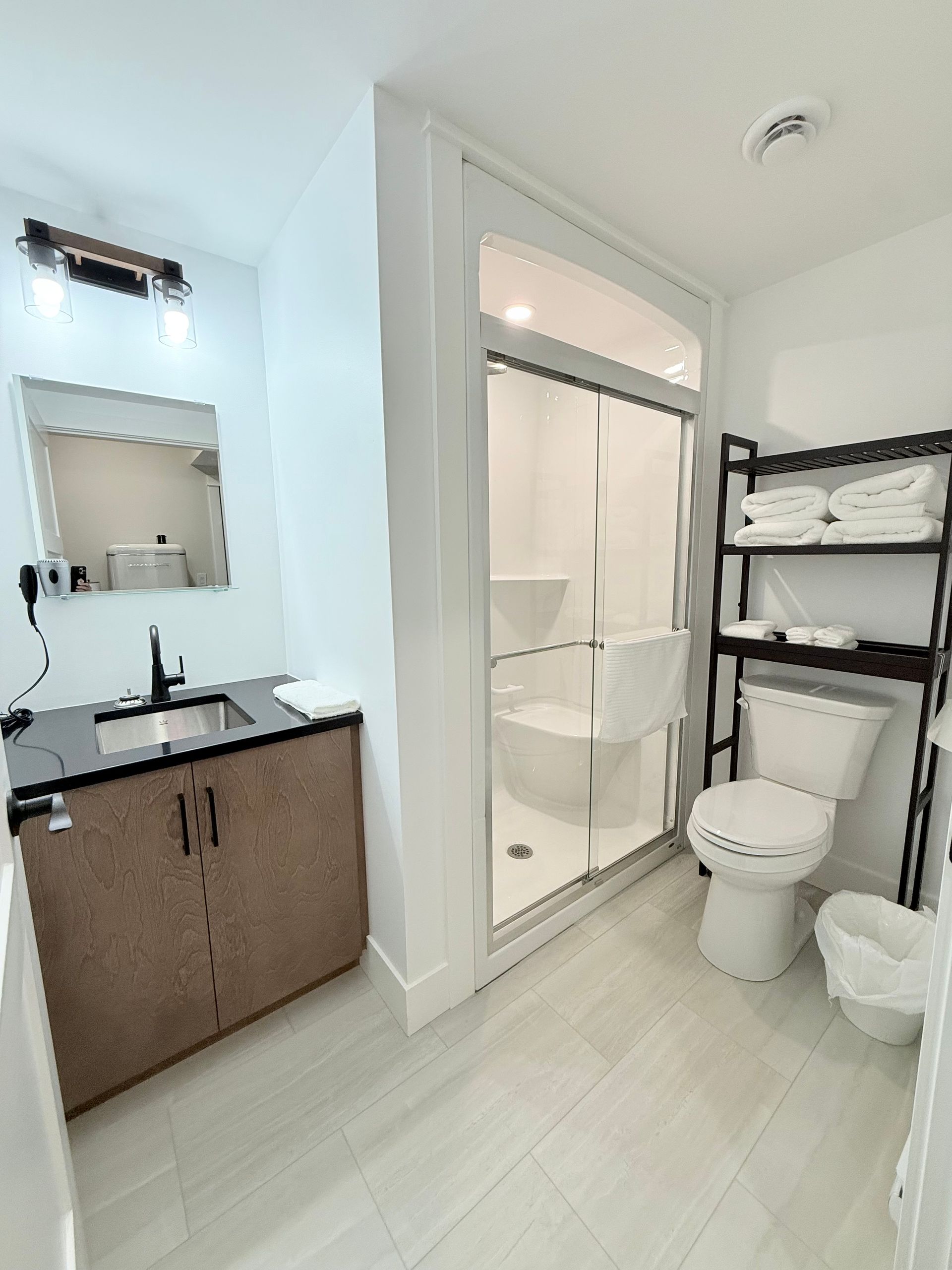 Bright modern bathroom with vanity, shower, toilet, and shelving unit