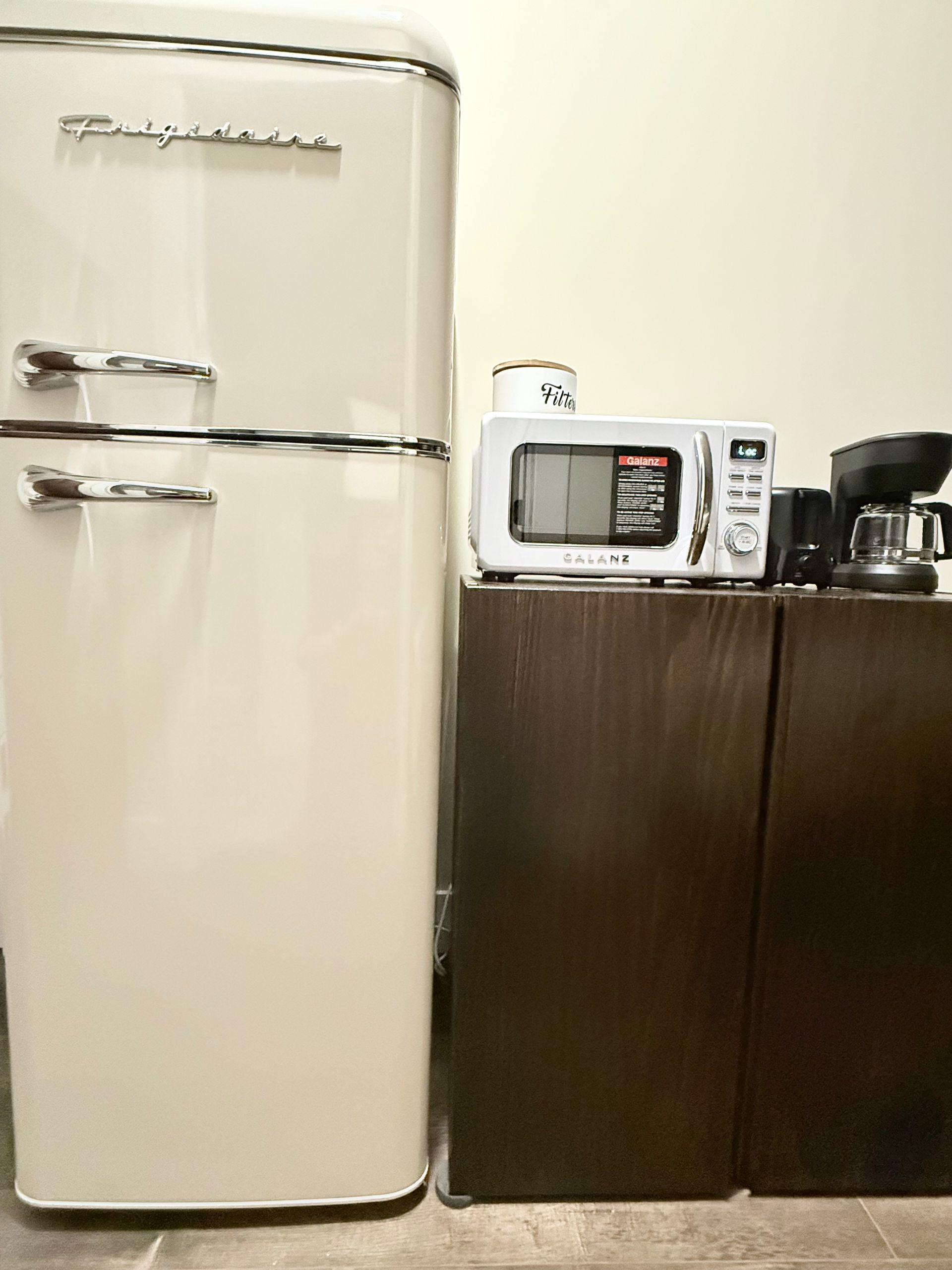 Small kitchen with a cream refrigerator, microwave on dark cabinets, and a coffee maker on the counter.