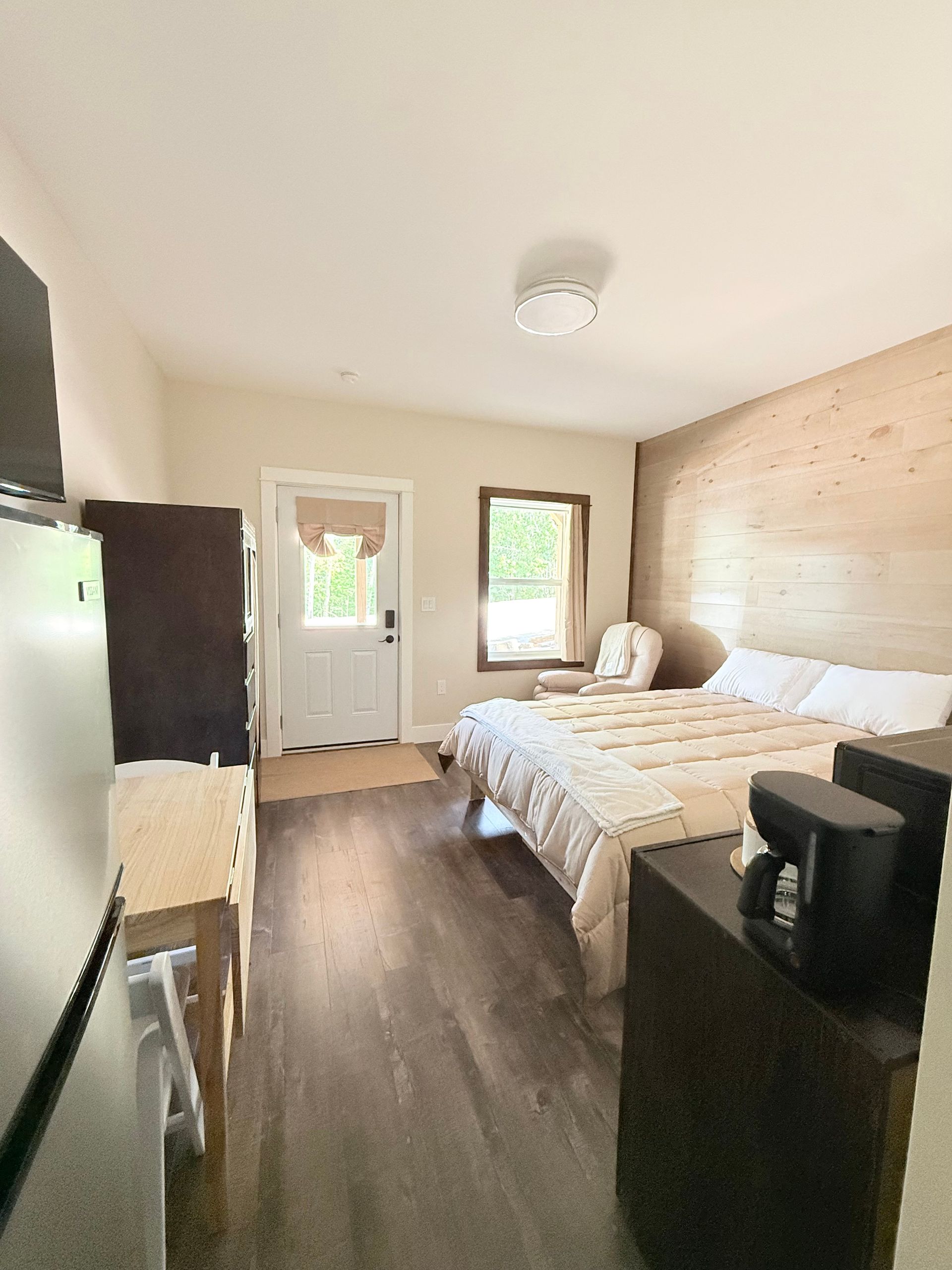 Small bedroom with bed, white door and window, wood floor, and light brick accent wall