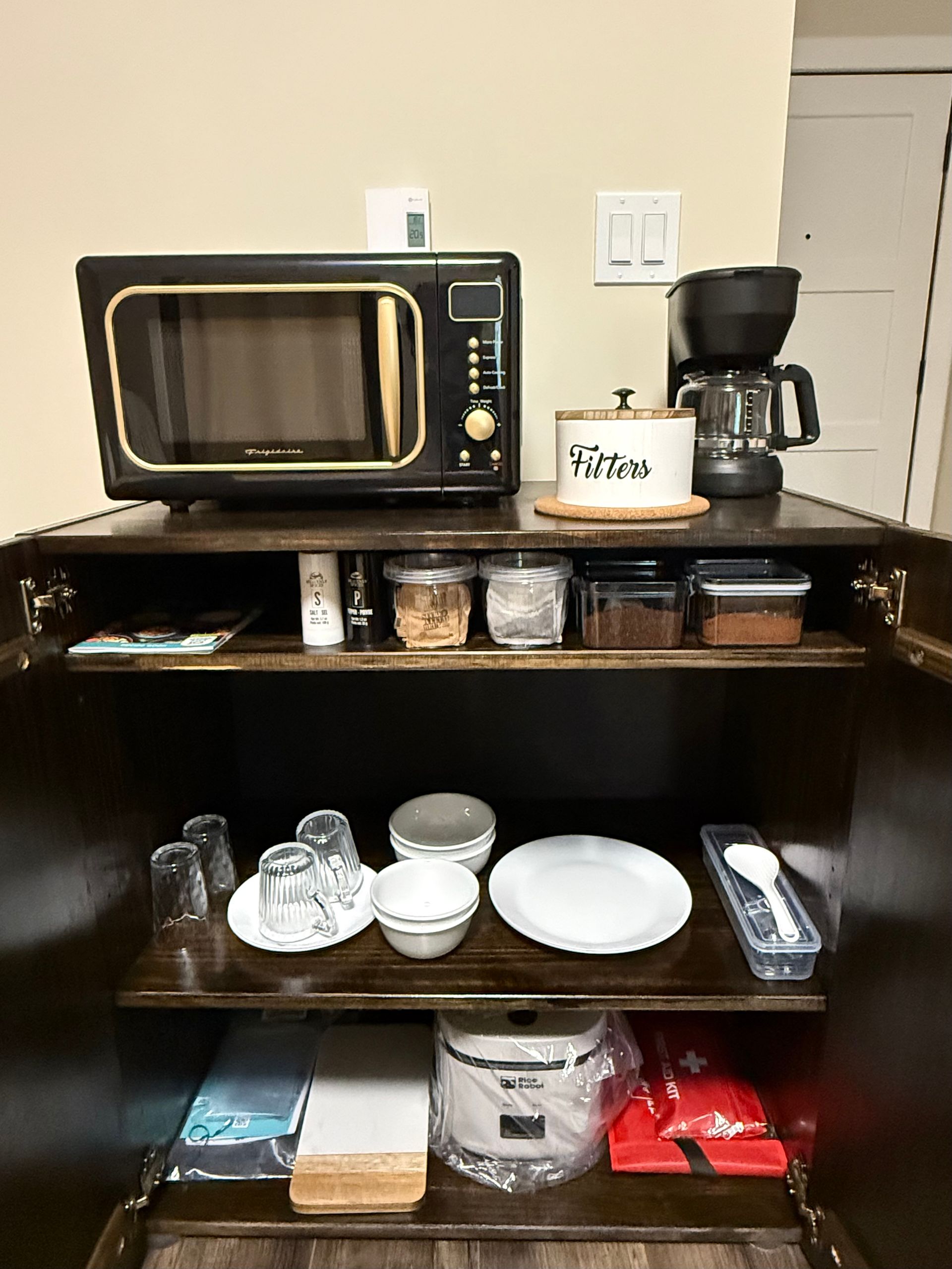 Break room shelf with microwave, coffee maker, mugs, plates, and condiments