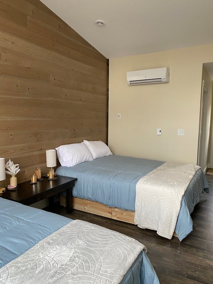 Small hotel room with two beds, wood accent wall, and wall-mounted air conditioner