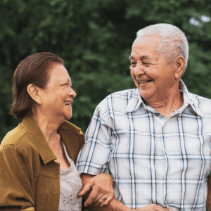 Two smiling people outdoors, laughing and holding each other’s arms in a green park.