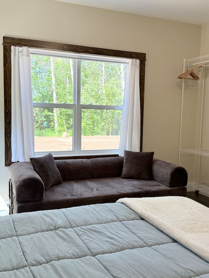 Bedroom with a dark sofa by a bright window and a bed in the foreground