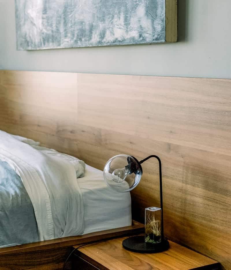 A bedroom with a bed, nightstand, lamp, and painting on the wall.
