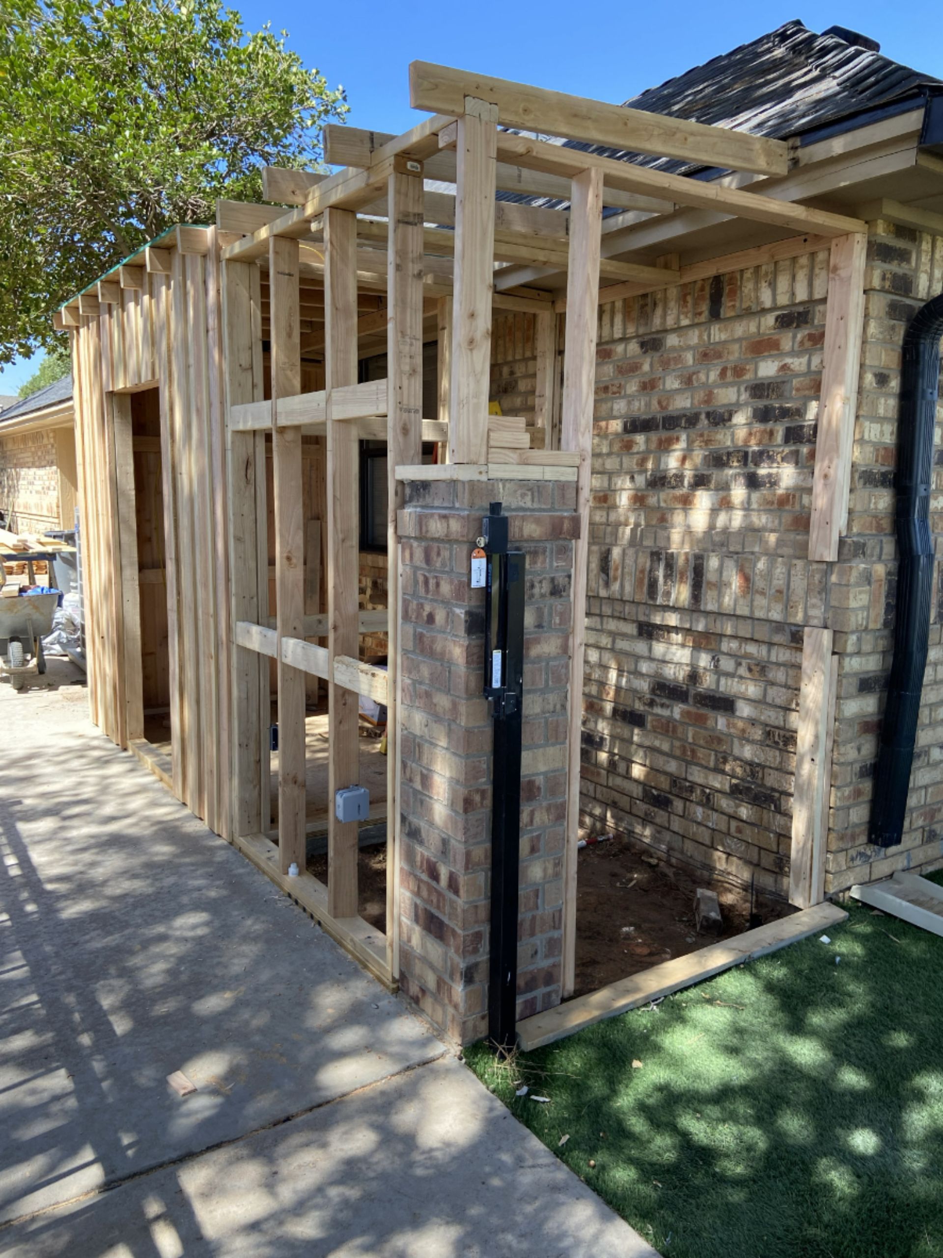 Wooden frame construction of an addition to a brick home. A black pipe runs along the brick.