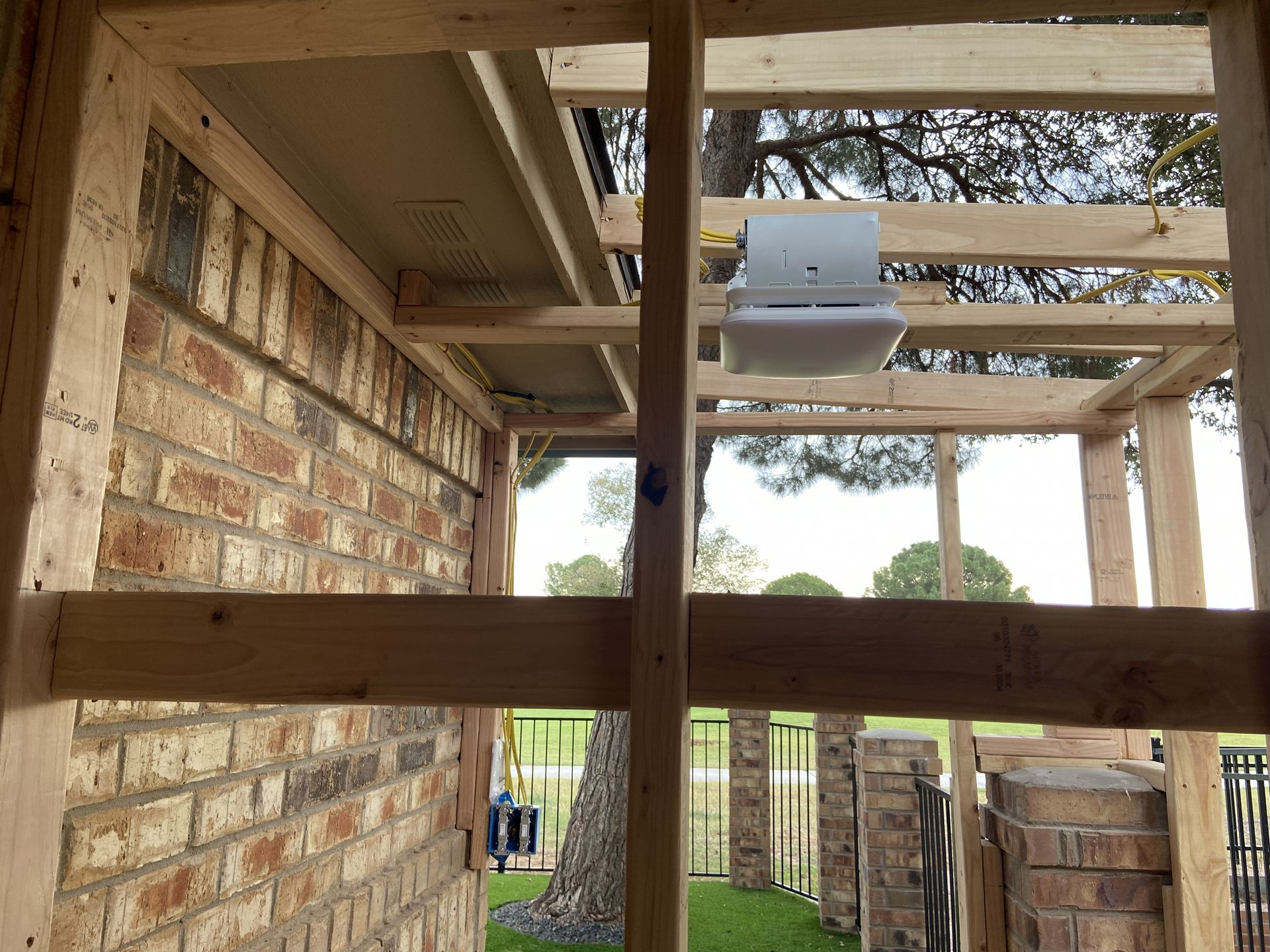 Wooden frame construction around brick wall. A/C unit visible inside. Trees and a lawn are in the background.
