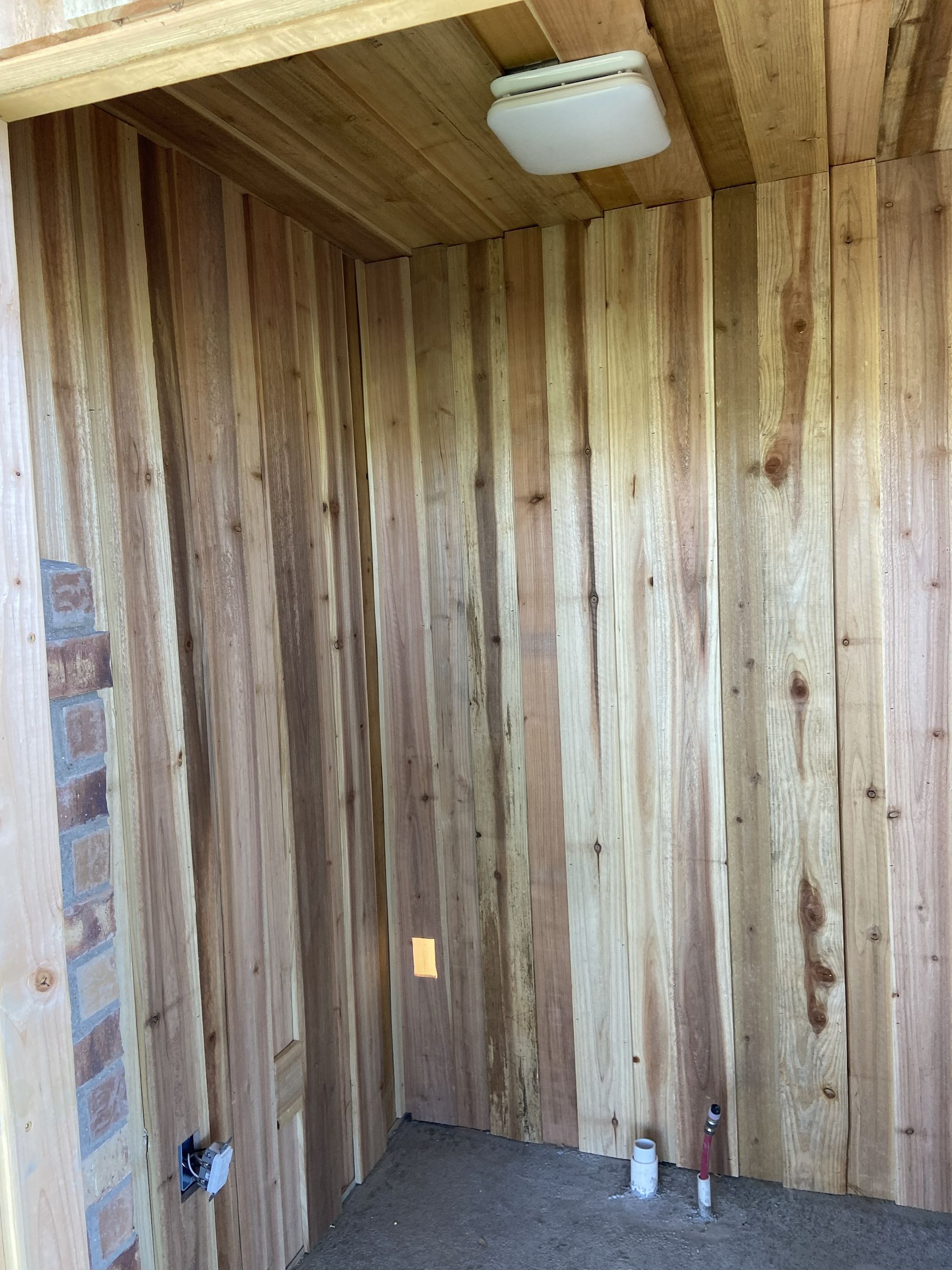 Wooden walls and ceiling in a small, unfinished room with a light fixture and electrical outlets.