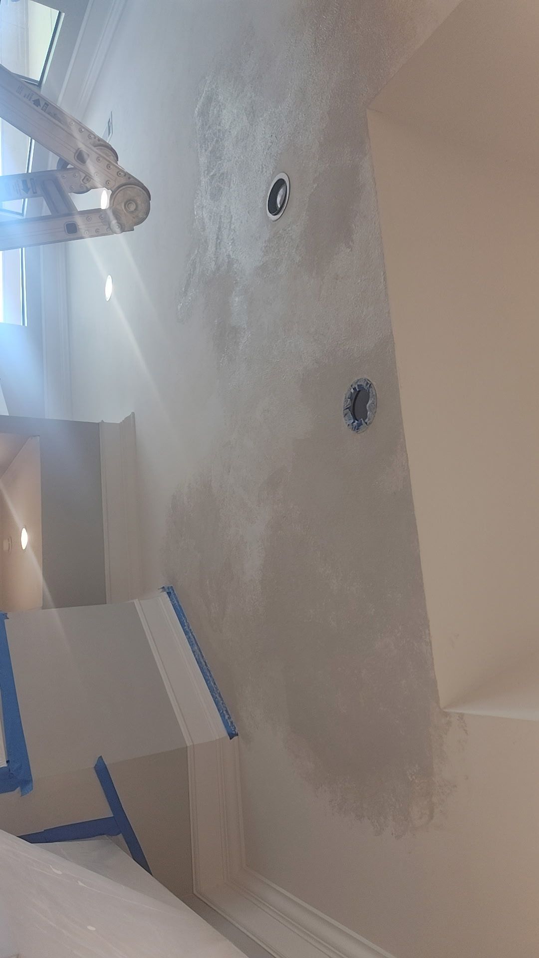 Wall being painted, showing electrical outlets. Painter using a roller; masking tape and ladder visible.