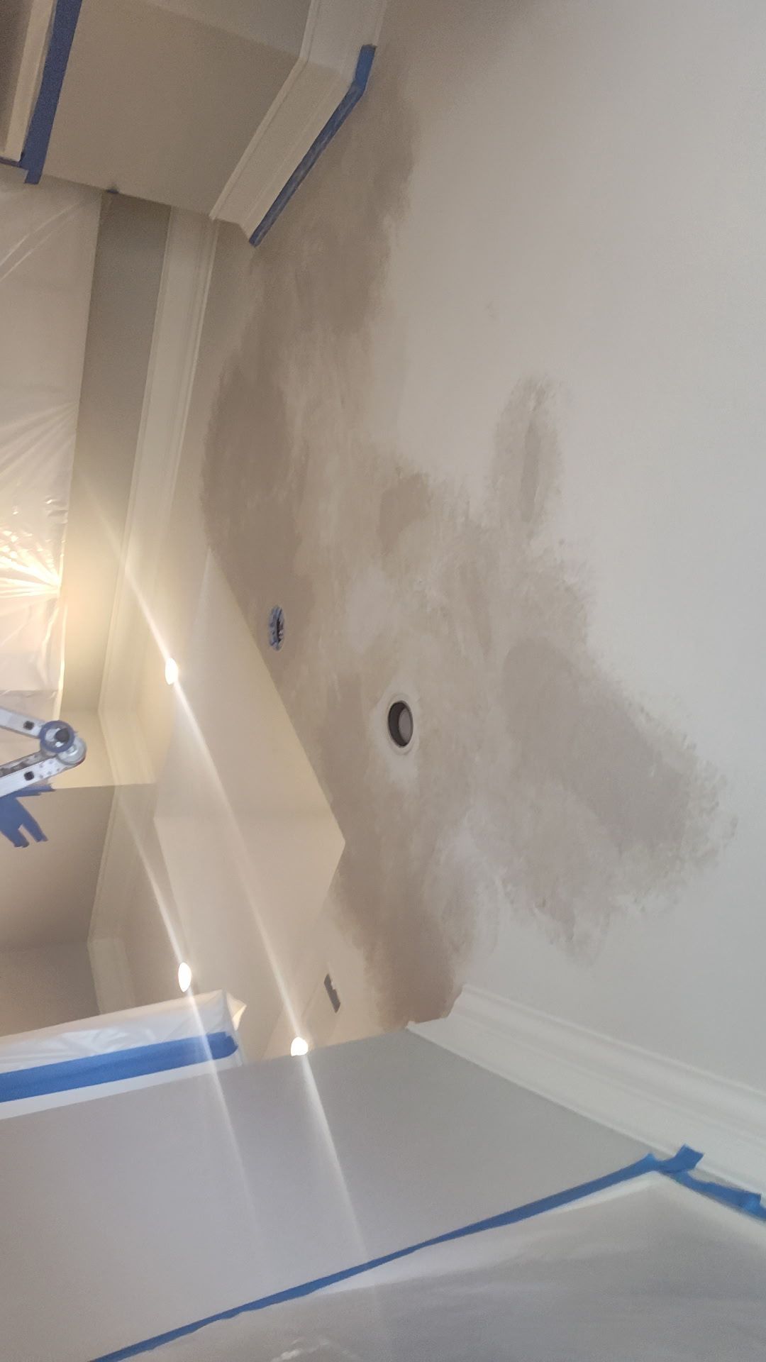 Room interior with drywall repair in progress. Sections of wall painted with grey primer. Electrical outlets are visible.