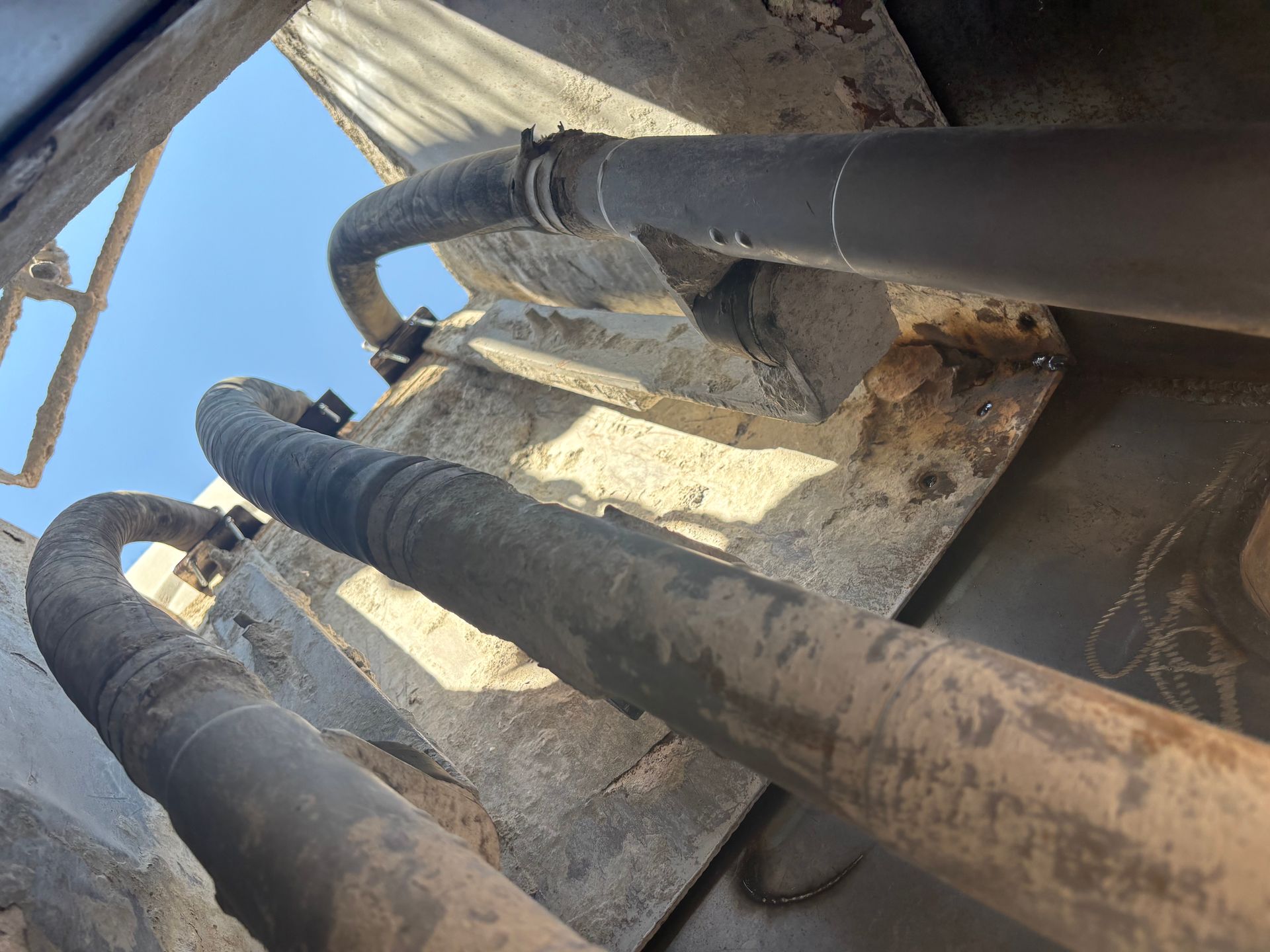 Three thick, gray, ribbed hoses secured to a metal surface, against a sky background.