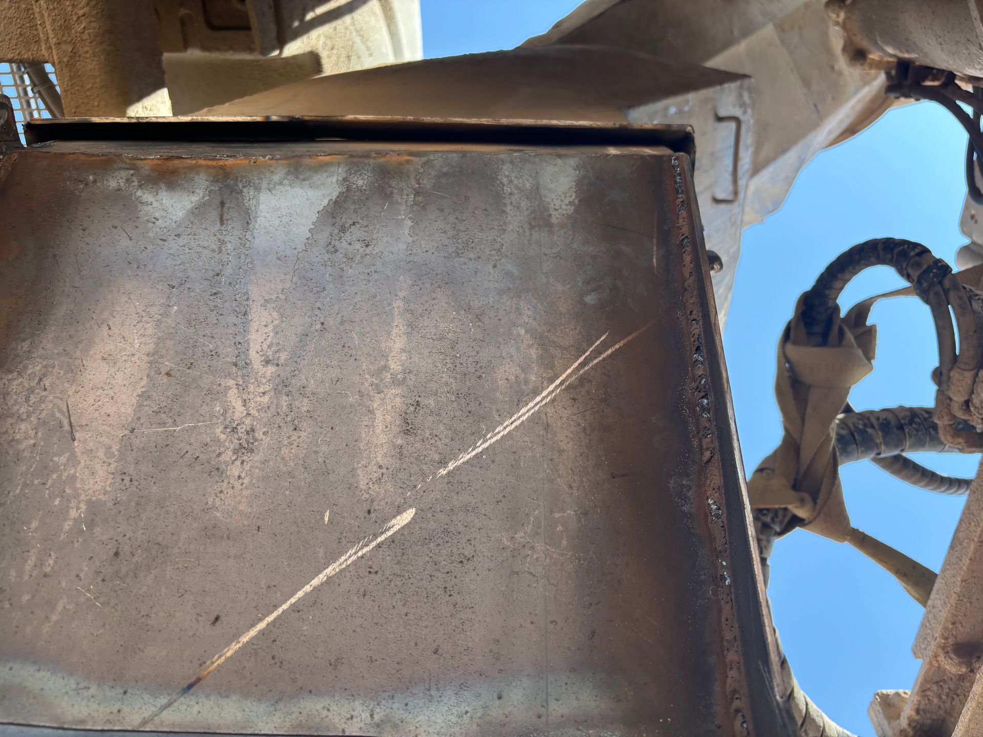Close-up of a weathered, rectangular metal component with scratches against a blue sky background.