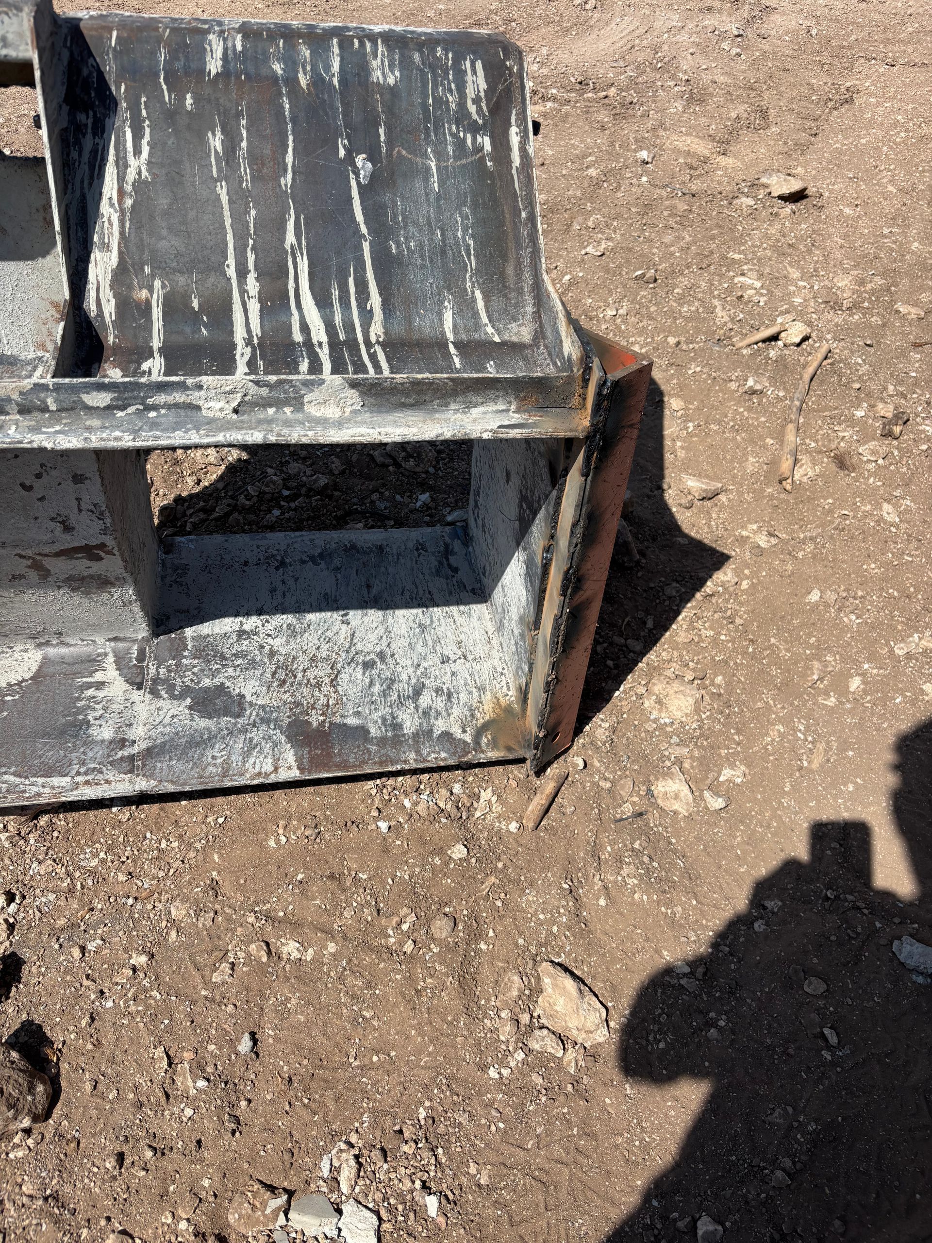 Black, weathered metal bucket on the ground, likely construction or industrial.