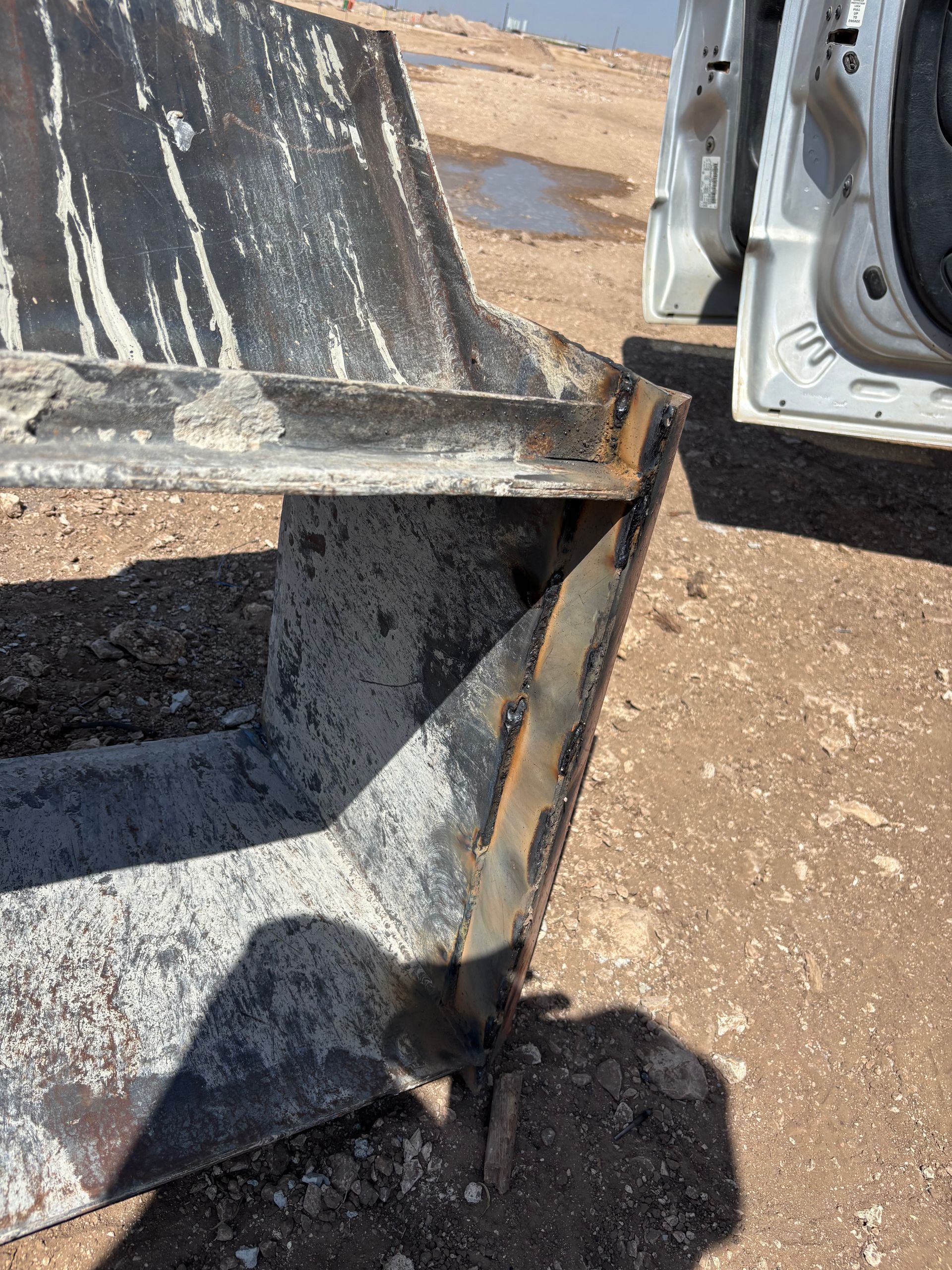 Close-up of a large, weathered metal structure with visible welds and a shadow cast on the ground.
