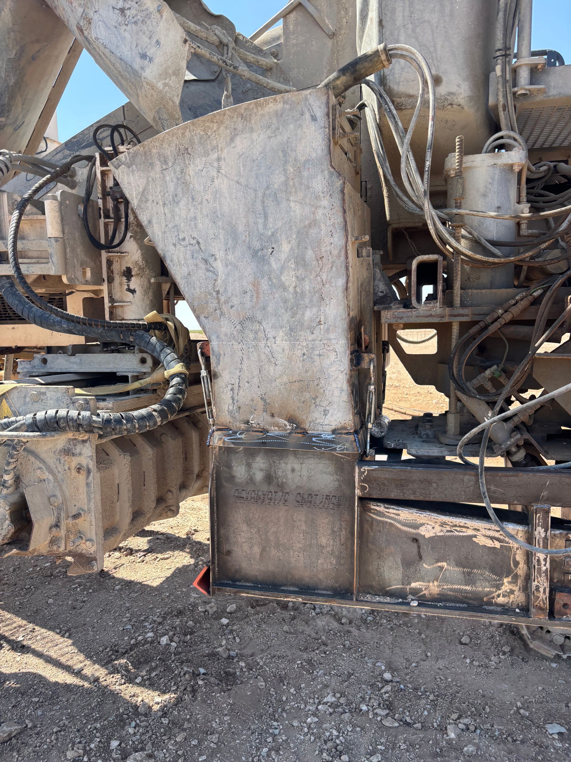 Close-up of industrial machinery, showing a metal chute welded to a rectangular base, outdoors on gravel.