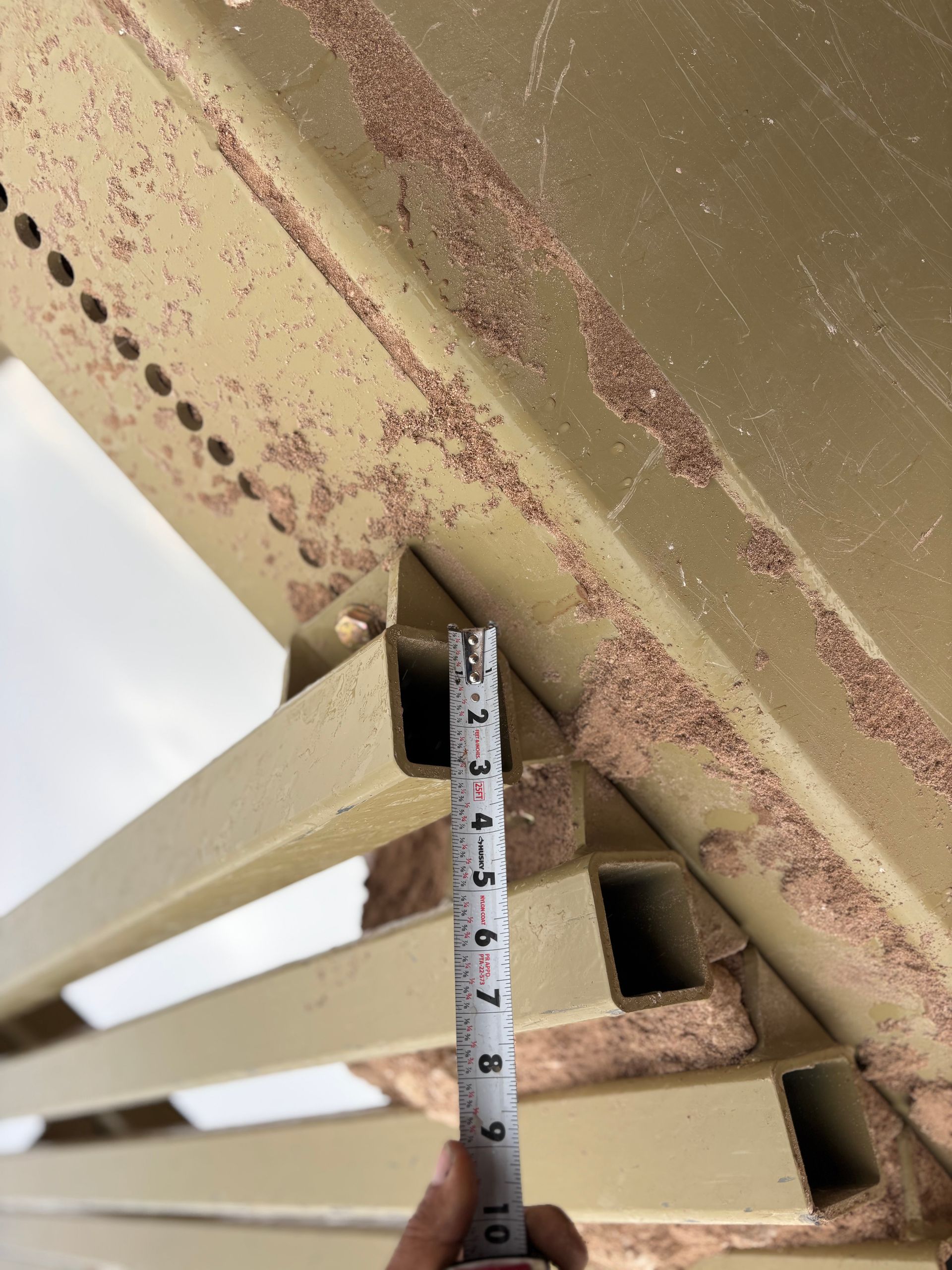 A person measures the space between metal beams with a tape measure.