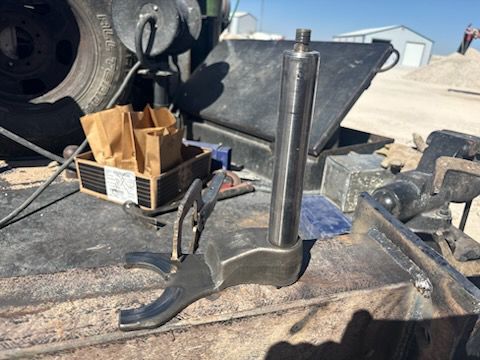 Metal machinery components sit on a surface outdoors, possibly being repaired. Brown paper bag visible.