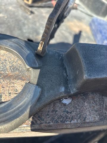Pliers holding a piece of black rubber or plastic, possibly a car part, with a circular element nearby.