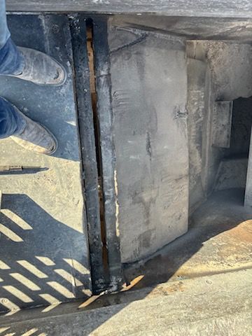 Top-down view of a dark metal grate and concrete structure, possibly part of a building's drainage system.