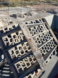 Metal grate with geometric cutouts, lying on its side outdoors.