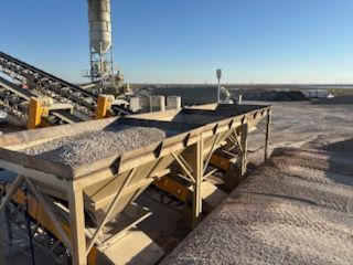 Concrete batch plant with conveyor belts and aggregate bins under a blue sky.