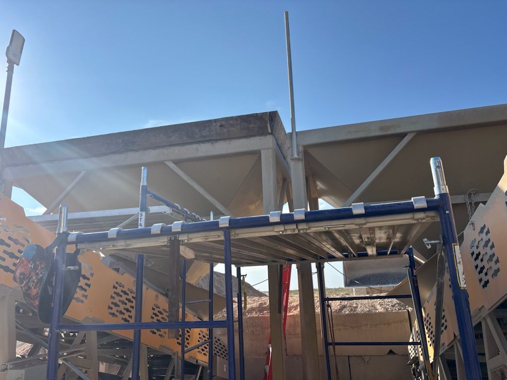 Scaffolding supports a building's roof with geometric panels. Bright sun and blue sky.