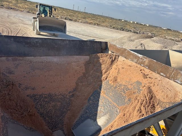 A front loader pushing brown material into a container at a quarry.