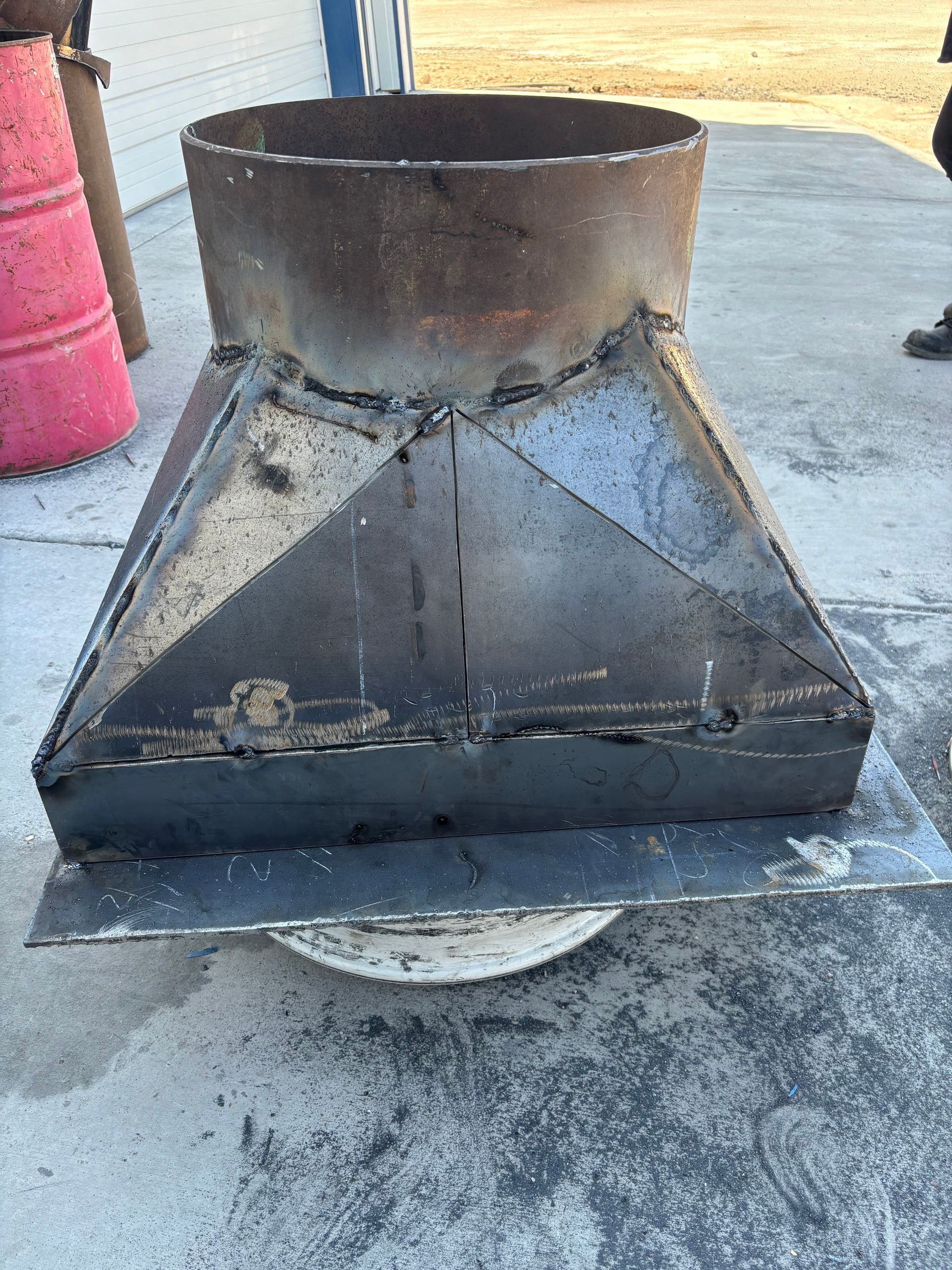 Metal chimney with a square base and a cylindrical top.