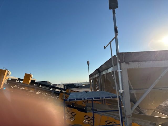 Yellow industrial equipment with conveyor belts, metal framework, and a blue sky in the background.