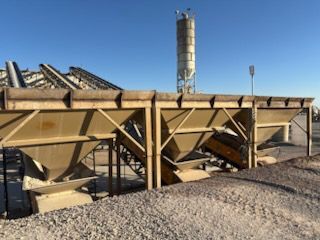Industrial concrete plant with storage bins and a silo under a blue sky.