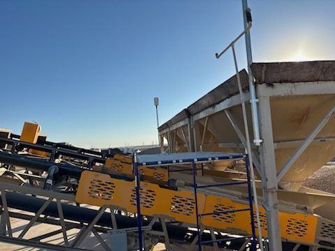 Conveyor belts with yellow safety guards under a sunny blue sky at an industrial site.