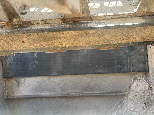 Black rectangular opening under a rusty metal beam, framed by concrete.