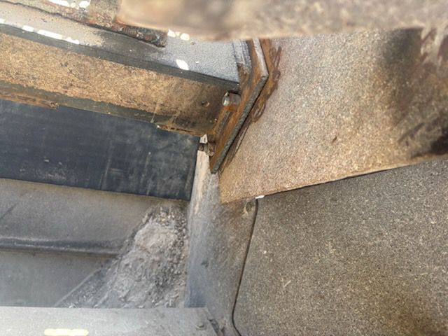 Rusty metal frame and bracket, possibly part of a vehicle's undercarriage, with visible bolts and dirt.