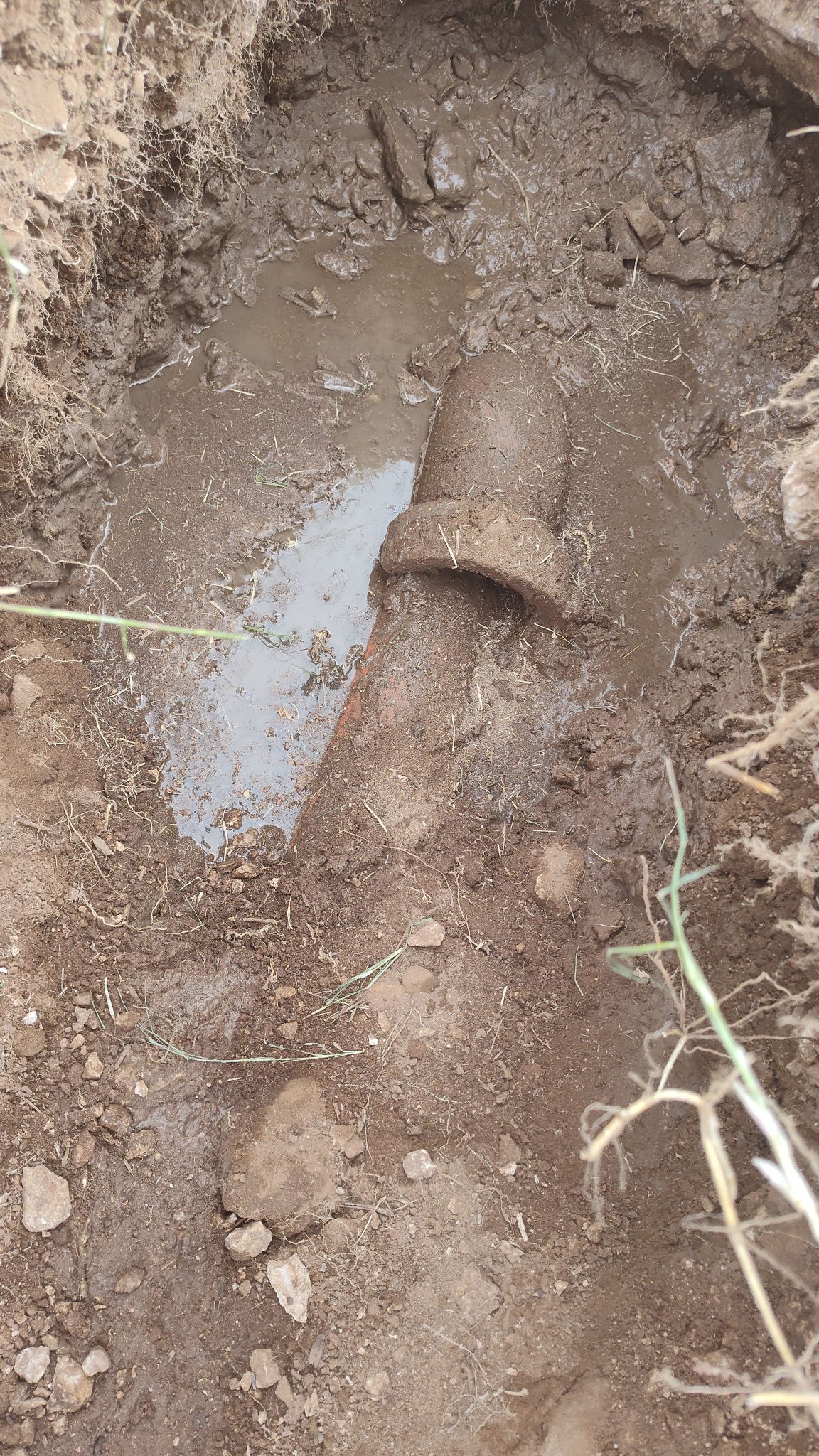 A section of buried pipe surrounded by muddy soil, pooling water.