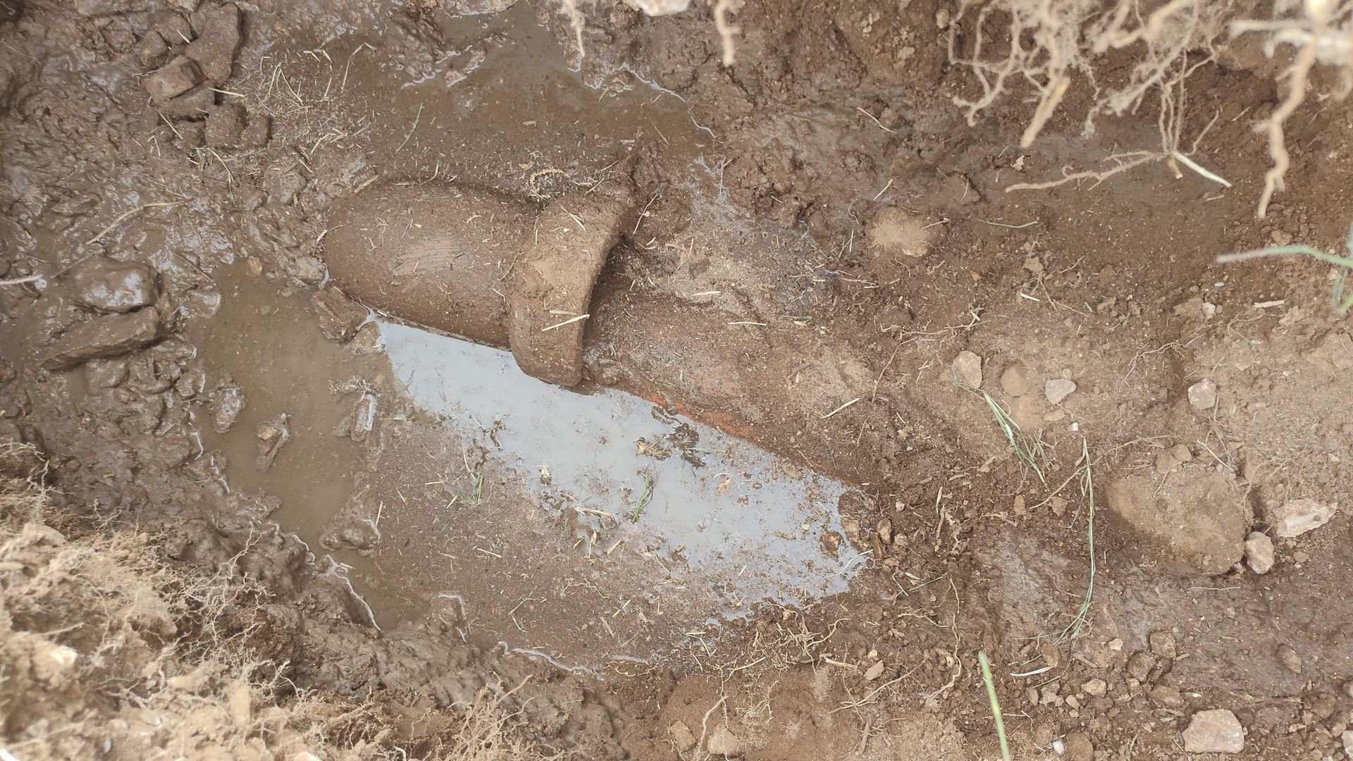 Pipe in a muddy hole in the ground; water surrounds the pipe.