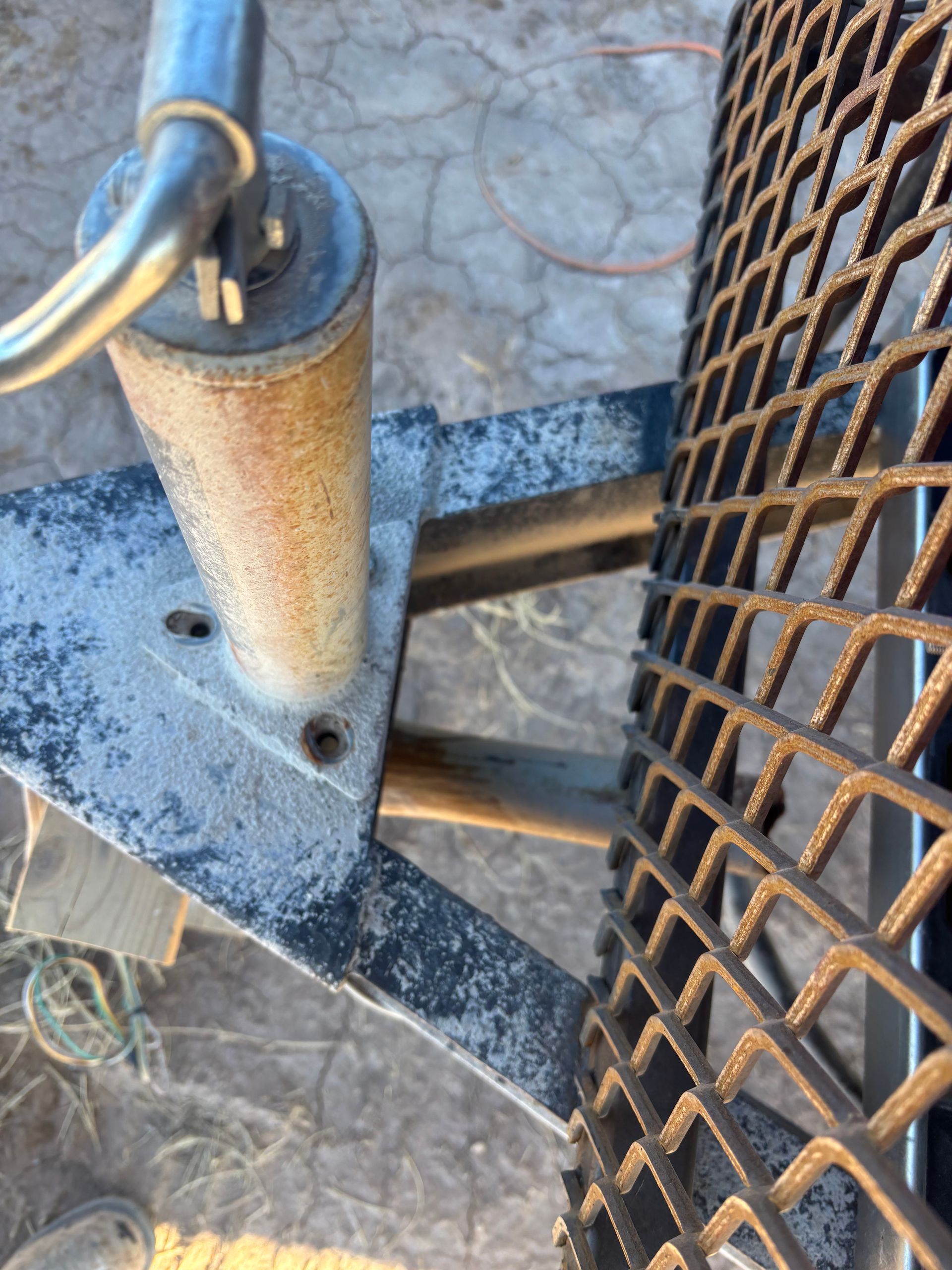 Trailer hitch and tire, with diamond mesh, metal frame, and ground in background.