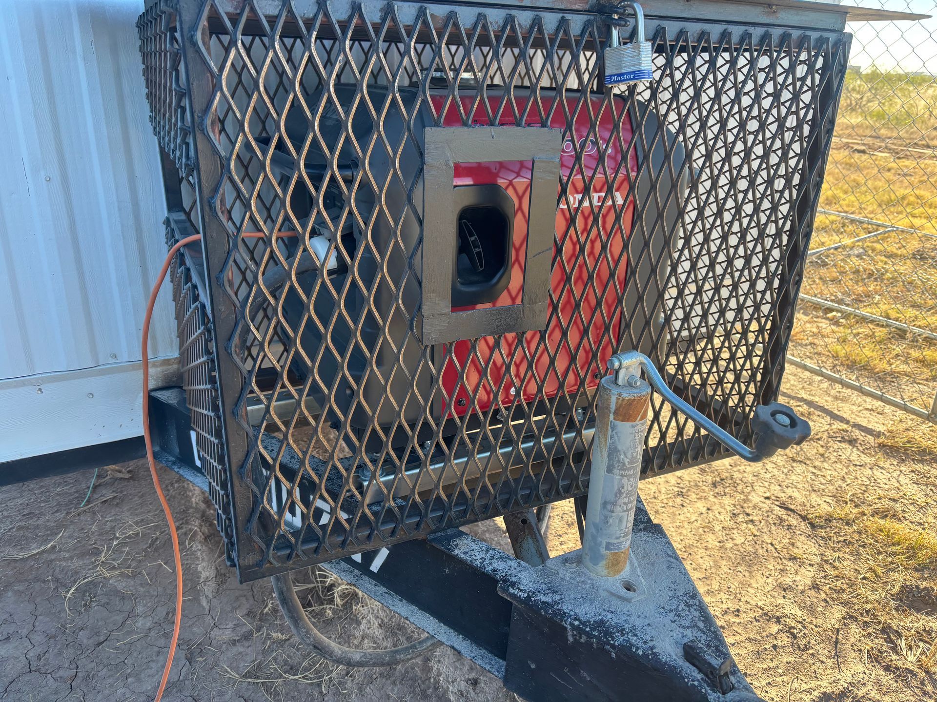 A red generator encased in a steel cage on a trailer, locked for security, in an outdoor setting.