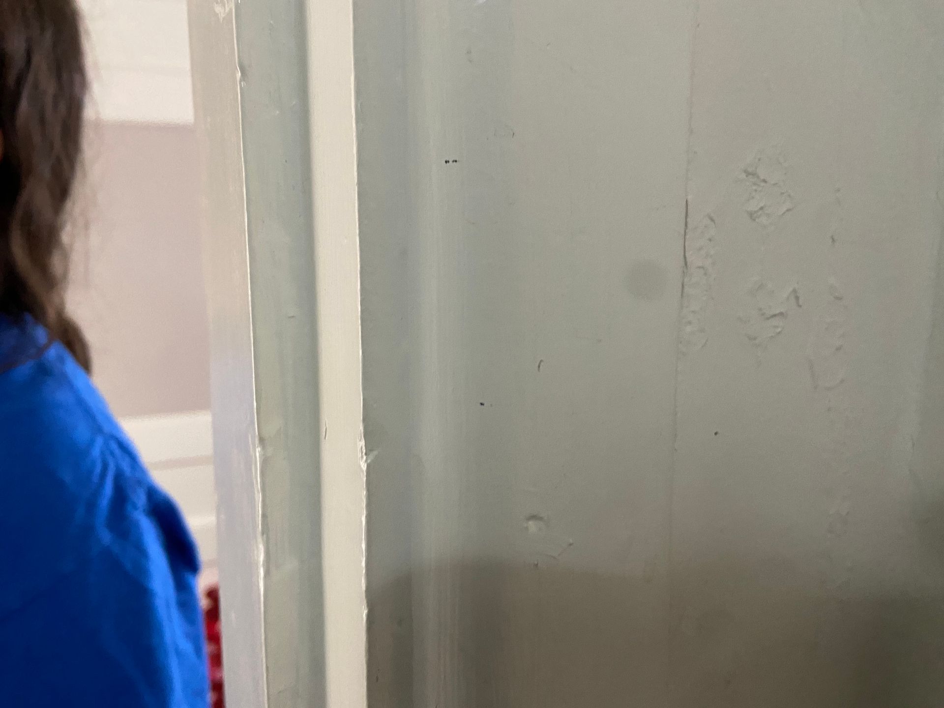 Person in blue shirt looks at a light-colored wall with visible imperfections and some dark spots.