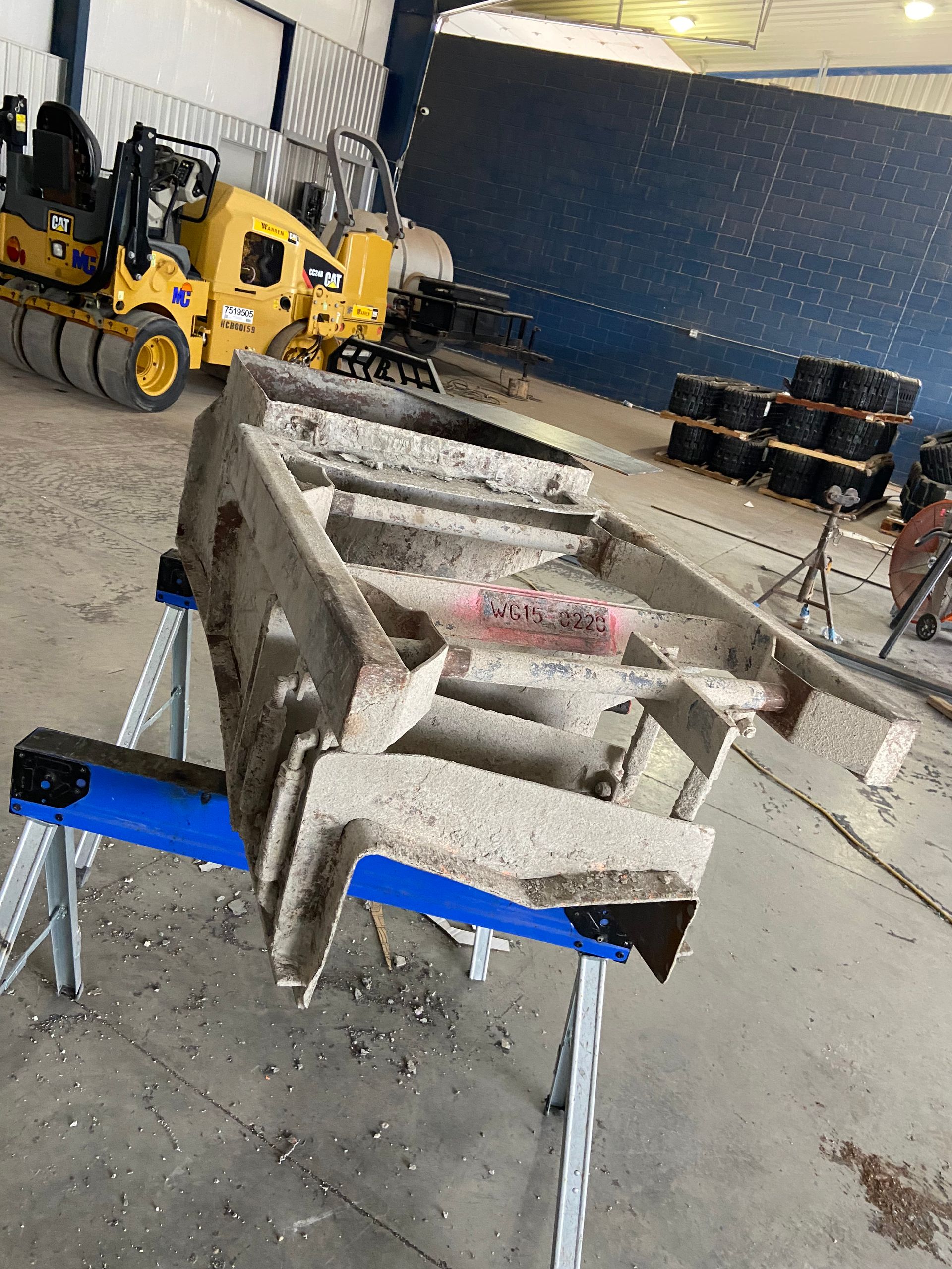 A concrete structure on blue sawhorses inside a warehouse, with construction equipment visible in the background.