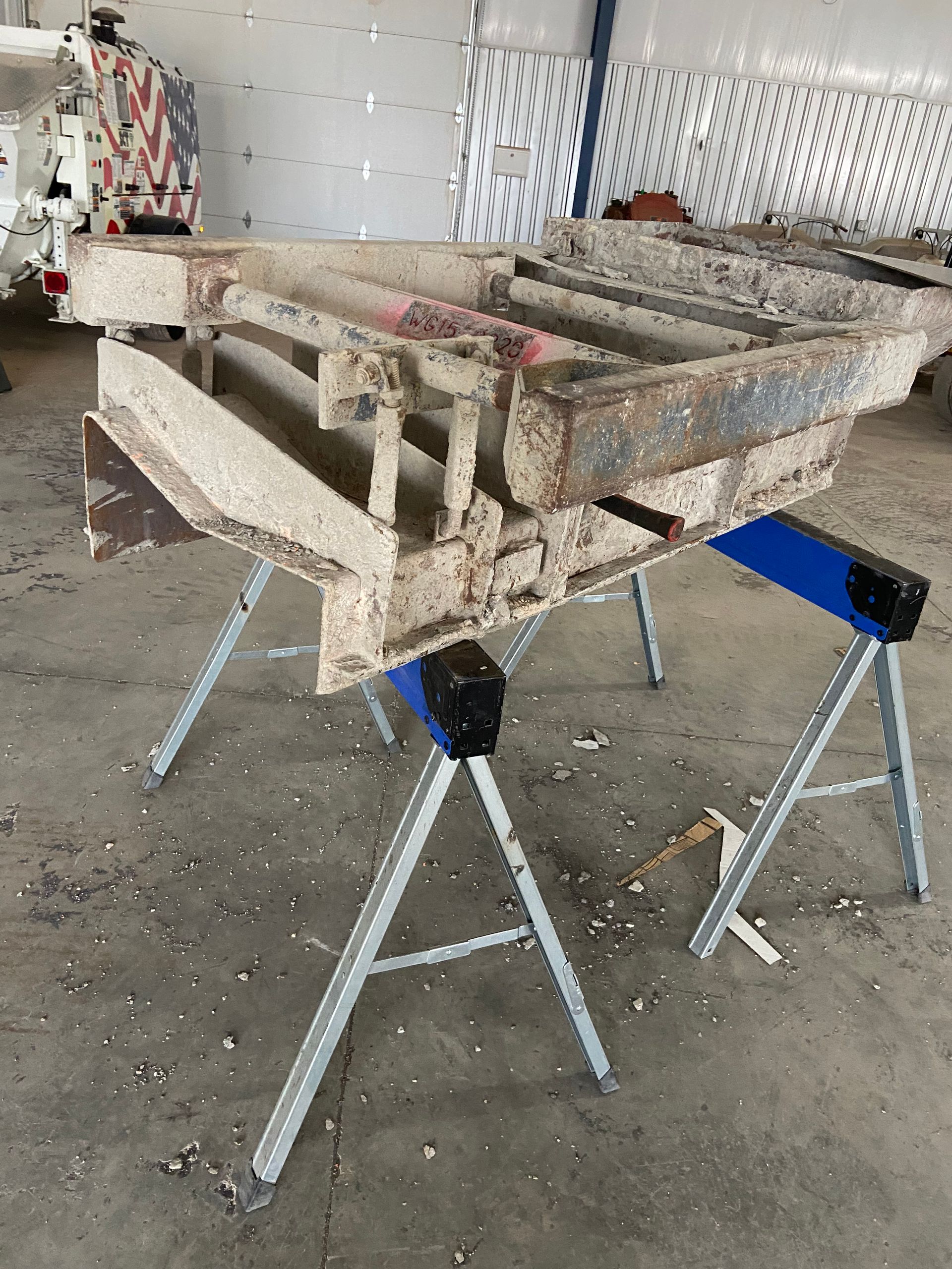 Metal frame on two blue sawhorses in a workshop setting.