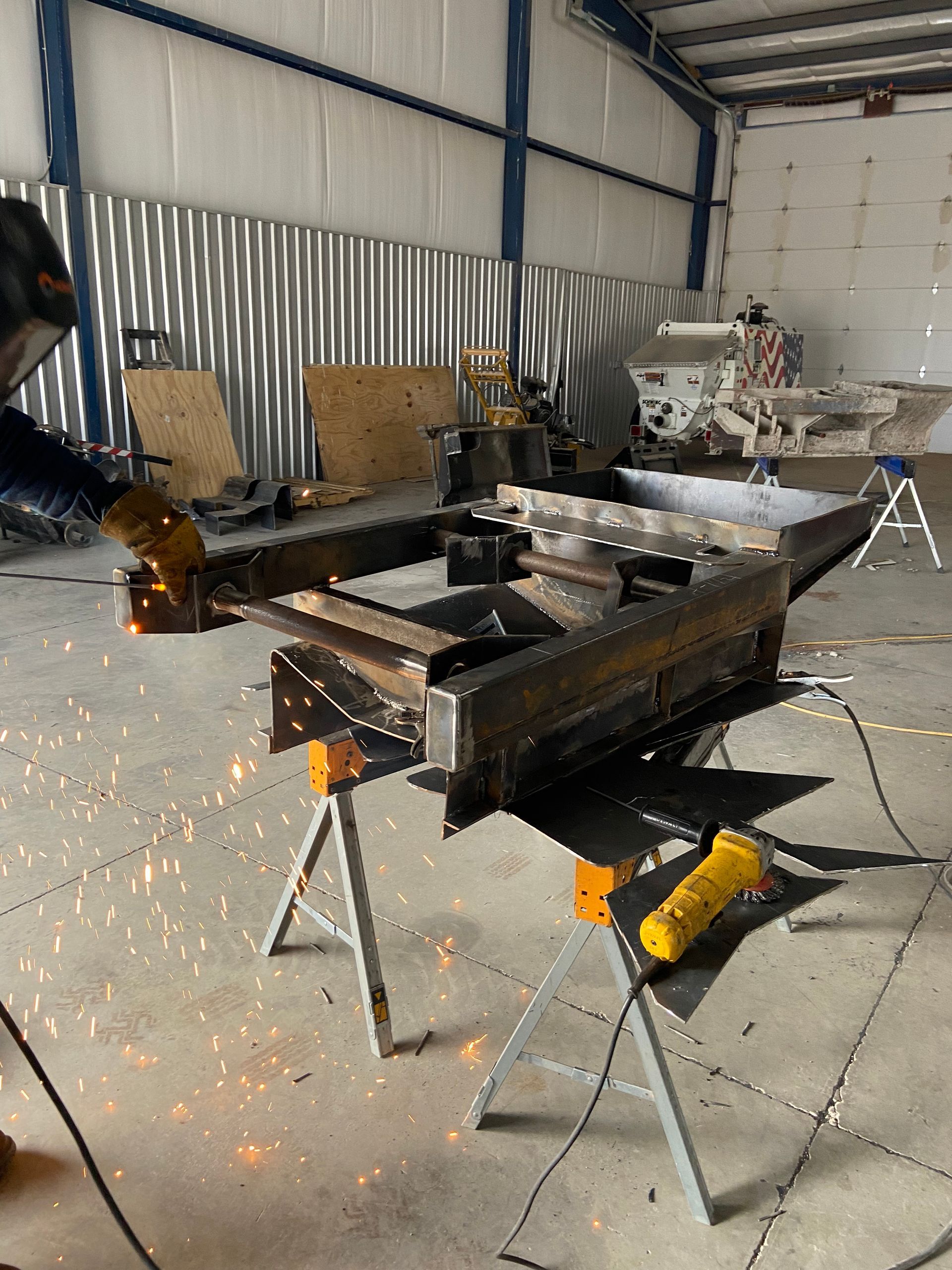 Person welding metal structure on sawhorse in workshop; sparks fly.