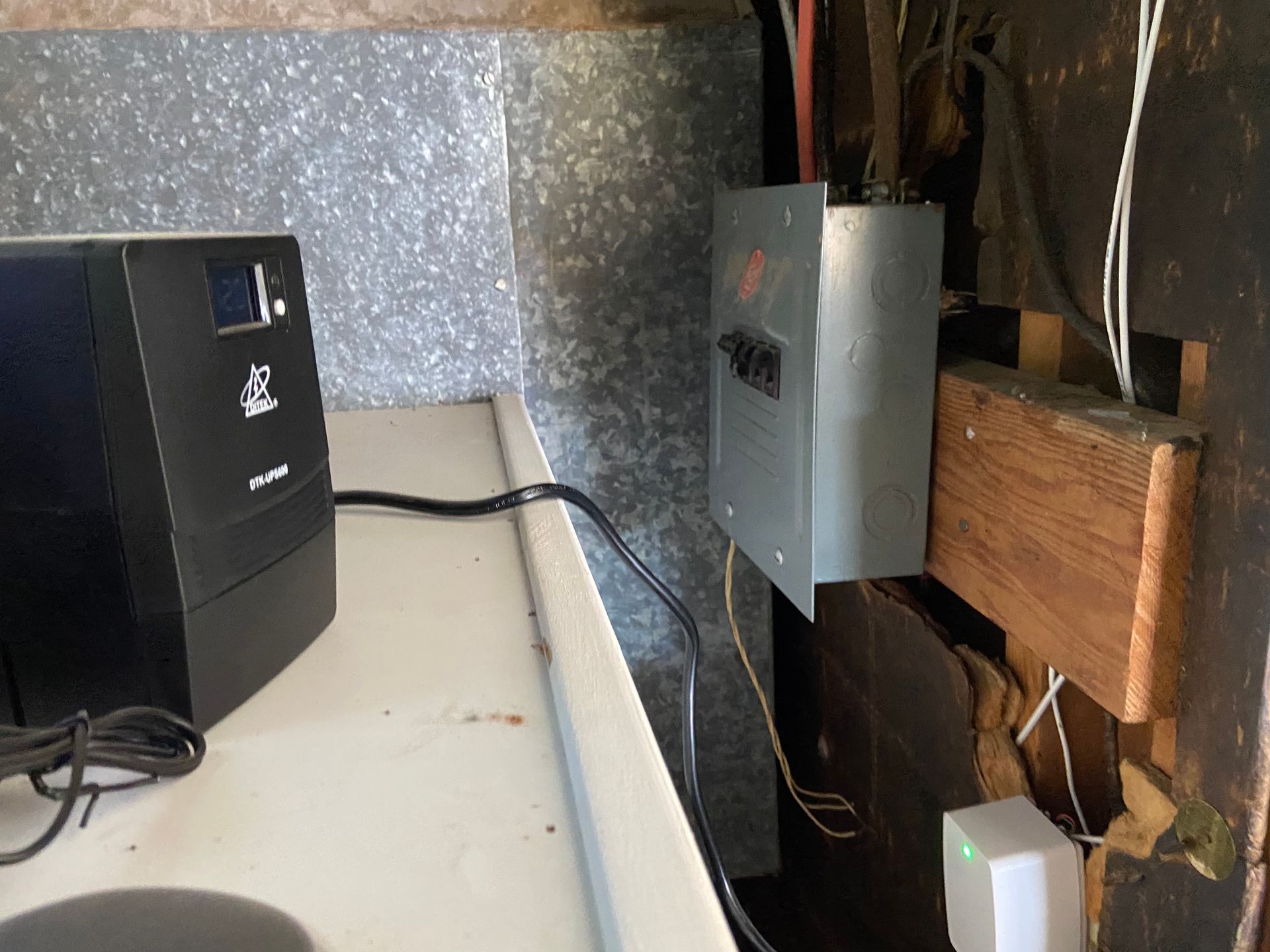 Black UPS and electrical panel on a white surface, attached to a wall with wires.