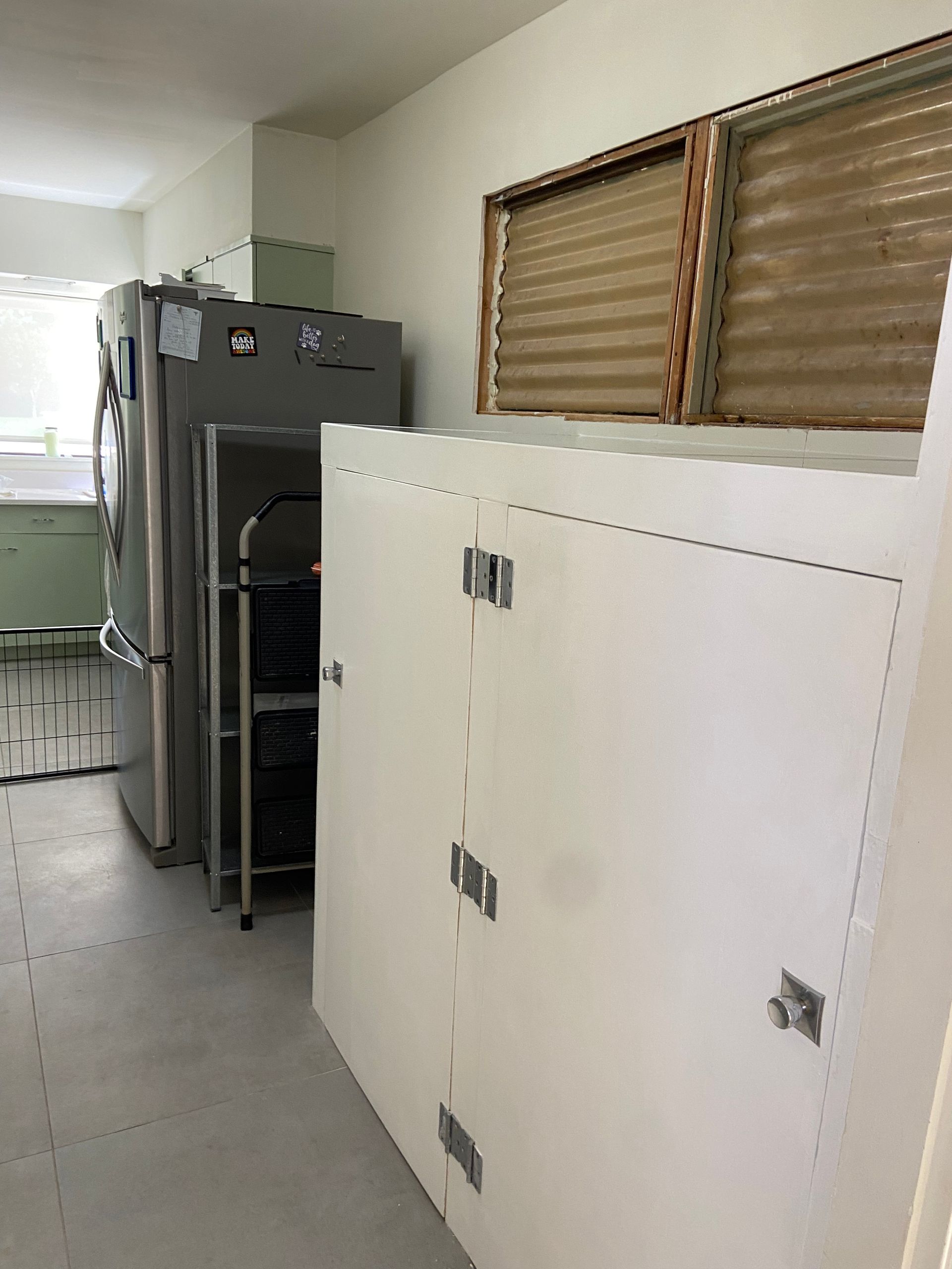 Kitchen with refrigerator, white cabinets, and a window with blinds.