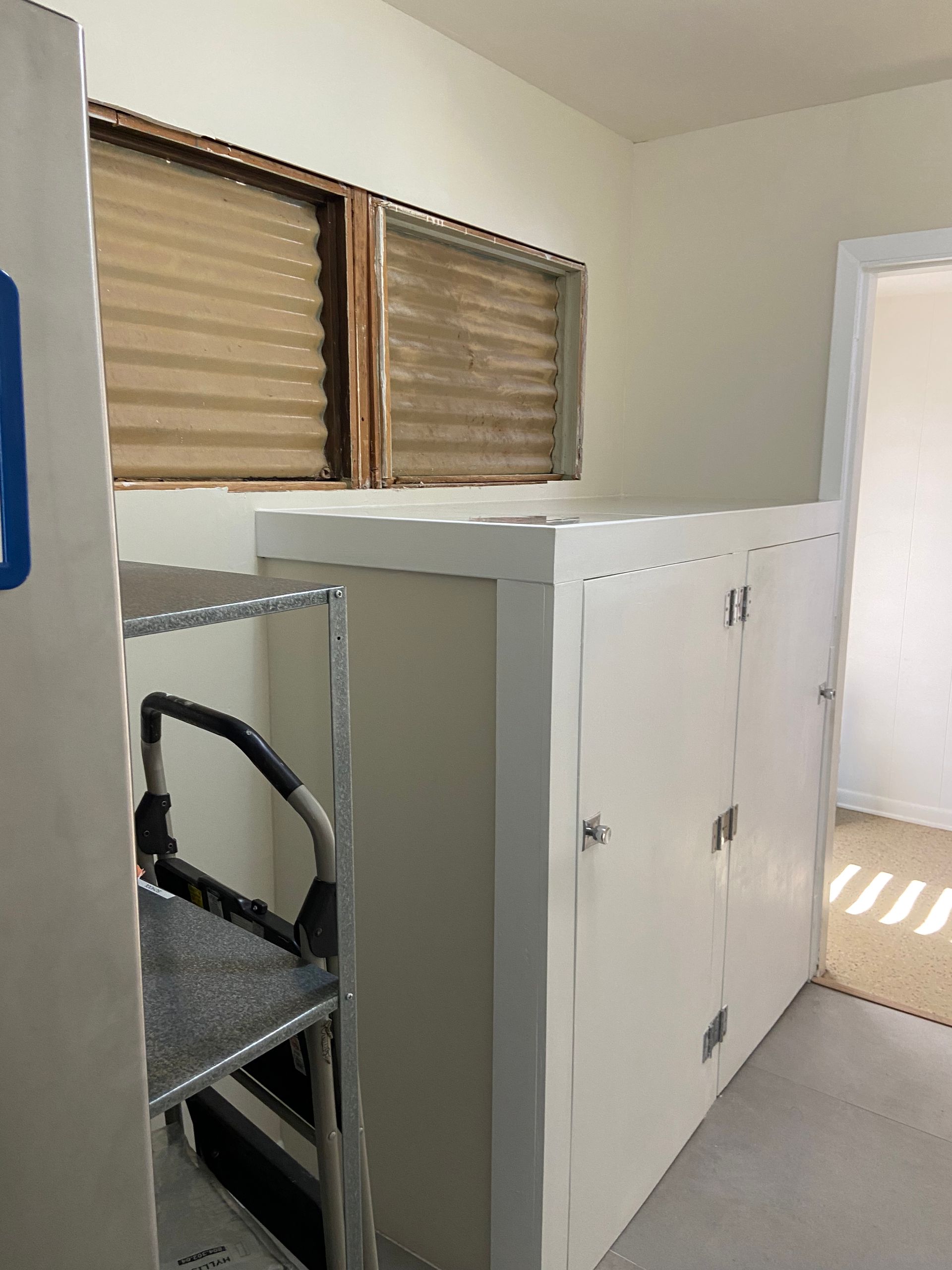 White cabinets with closed doors and a step stool next to a window with blinds.