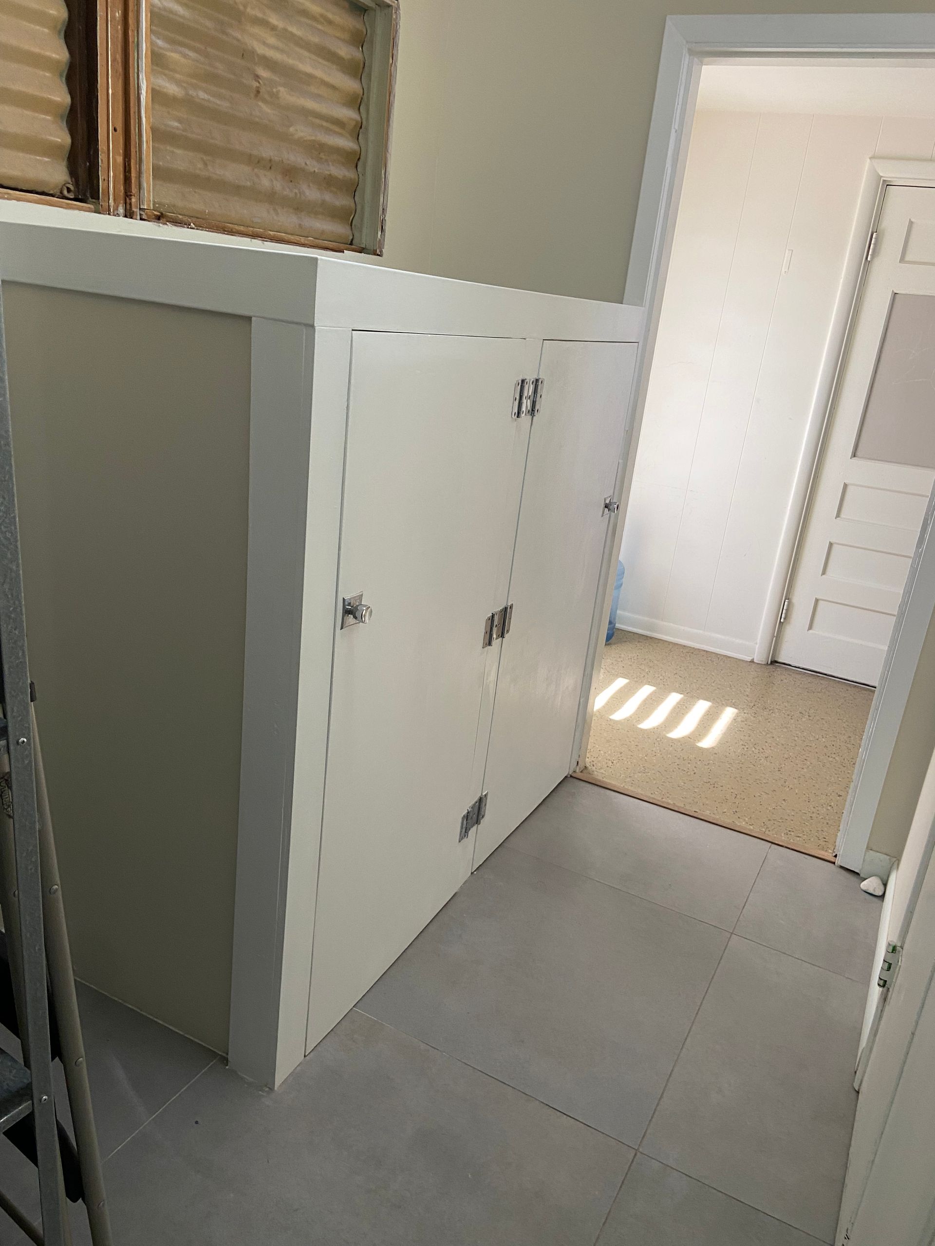 White cabinet with two doors in a room with light gray tile flooring, near an open doorway.