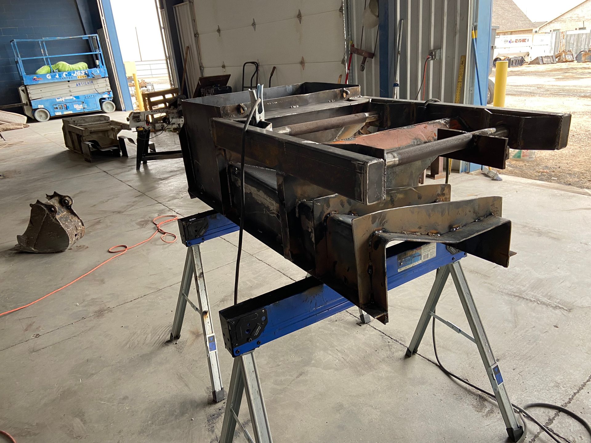 Welded metal structure on blue sawhorses in a warehouse.