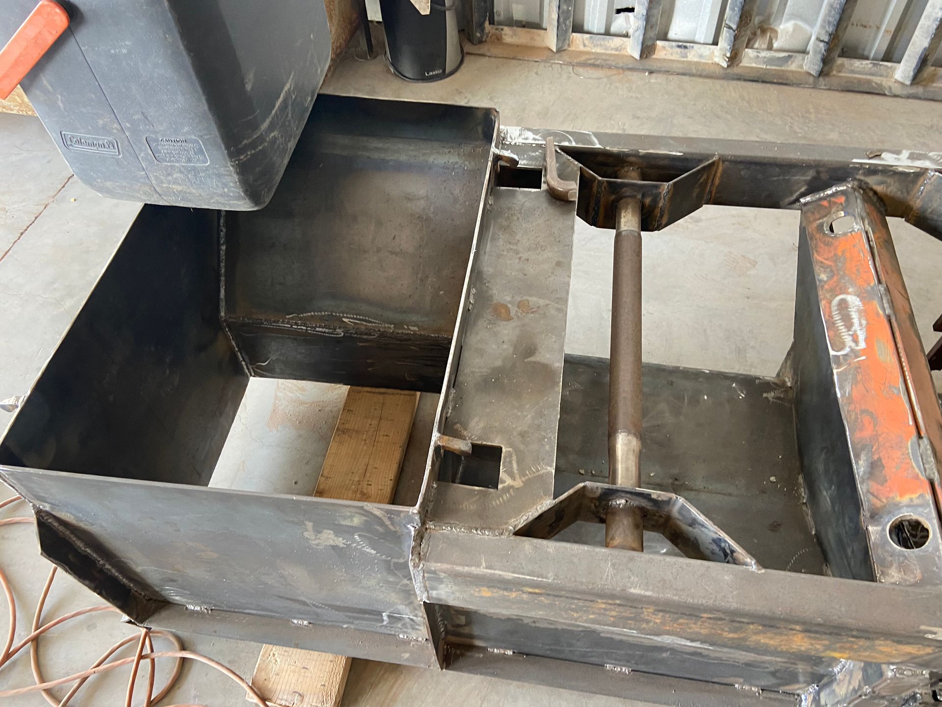 Metal fabrication project with a large bin-like structure and supporting framework. A bucket is nearby.