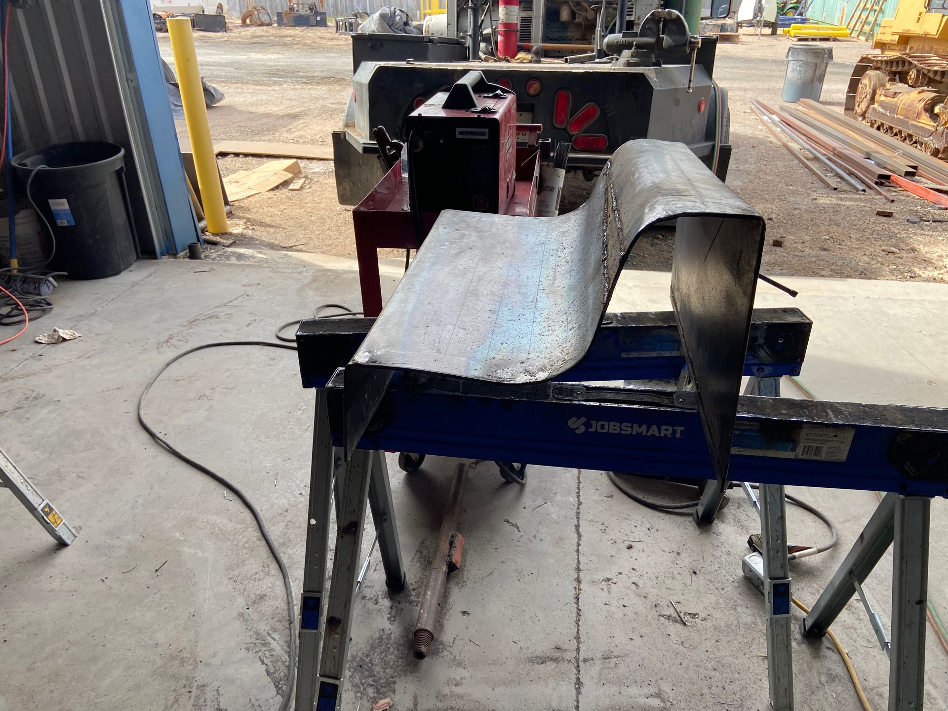 Metal sheet on sawhorse, possibly shaped with a bending machine, in a workshop setting.