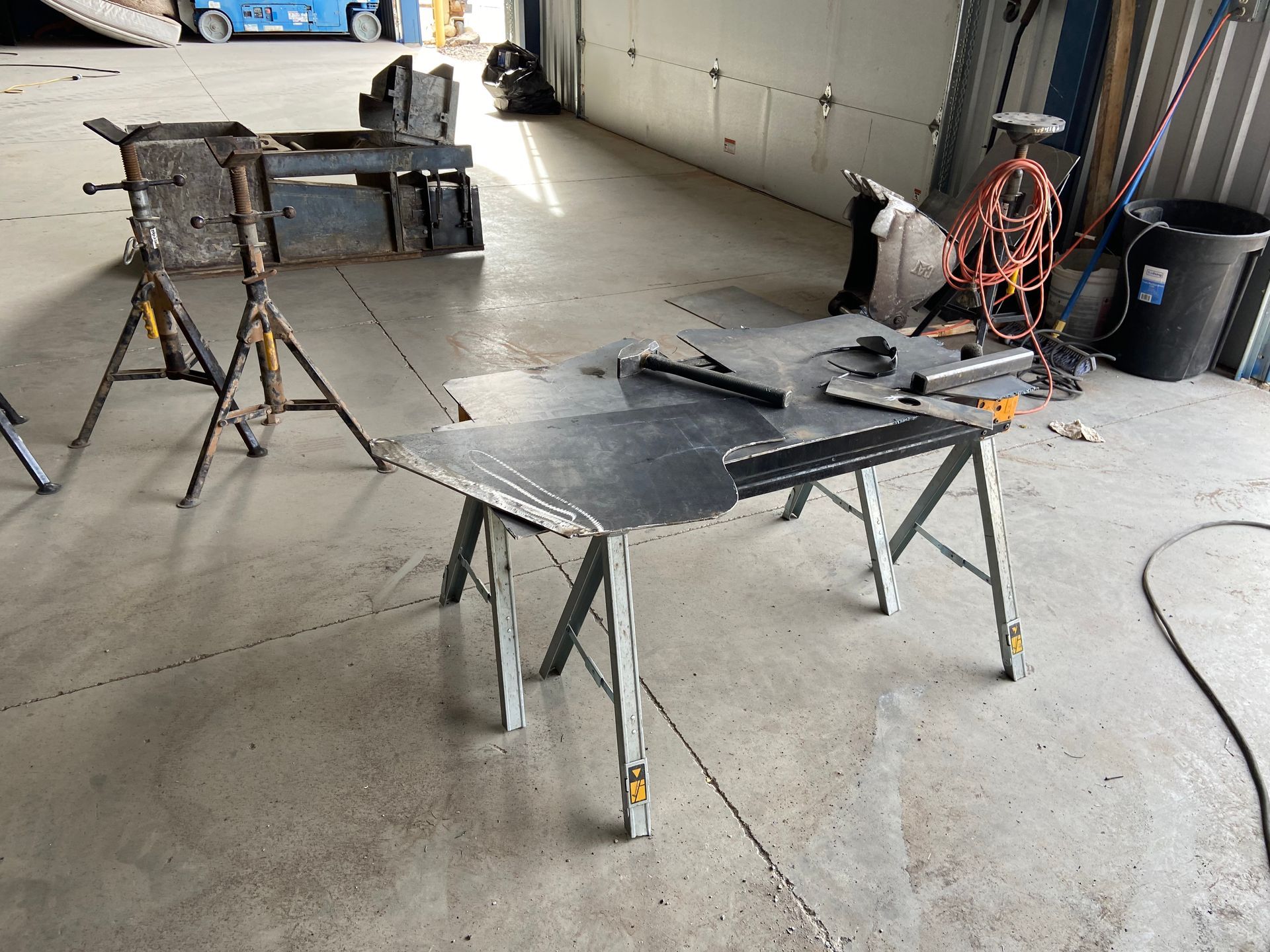 Metalworking shop with two sawhorses supporting metal sheets and tools on the floor.
