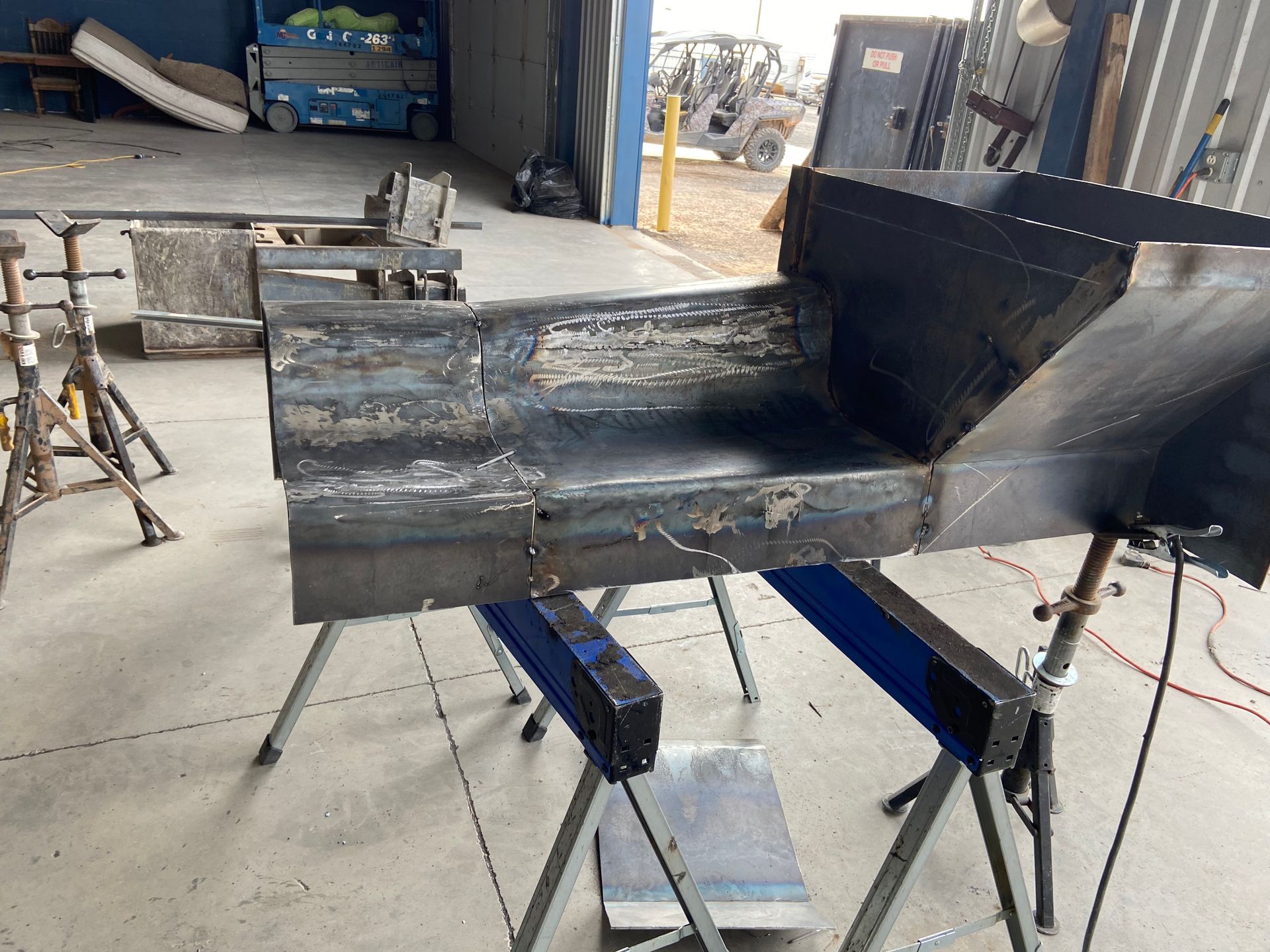 Welded metal structure in a workshop, supported by sawhorses.