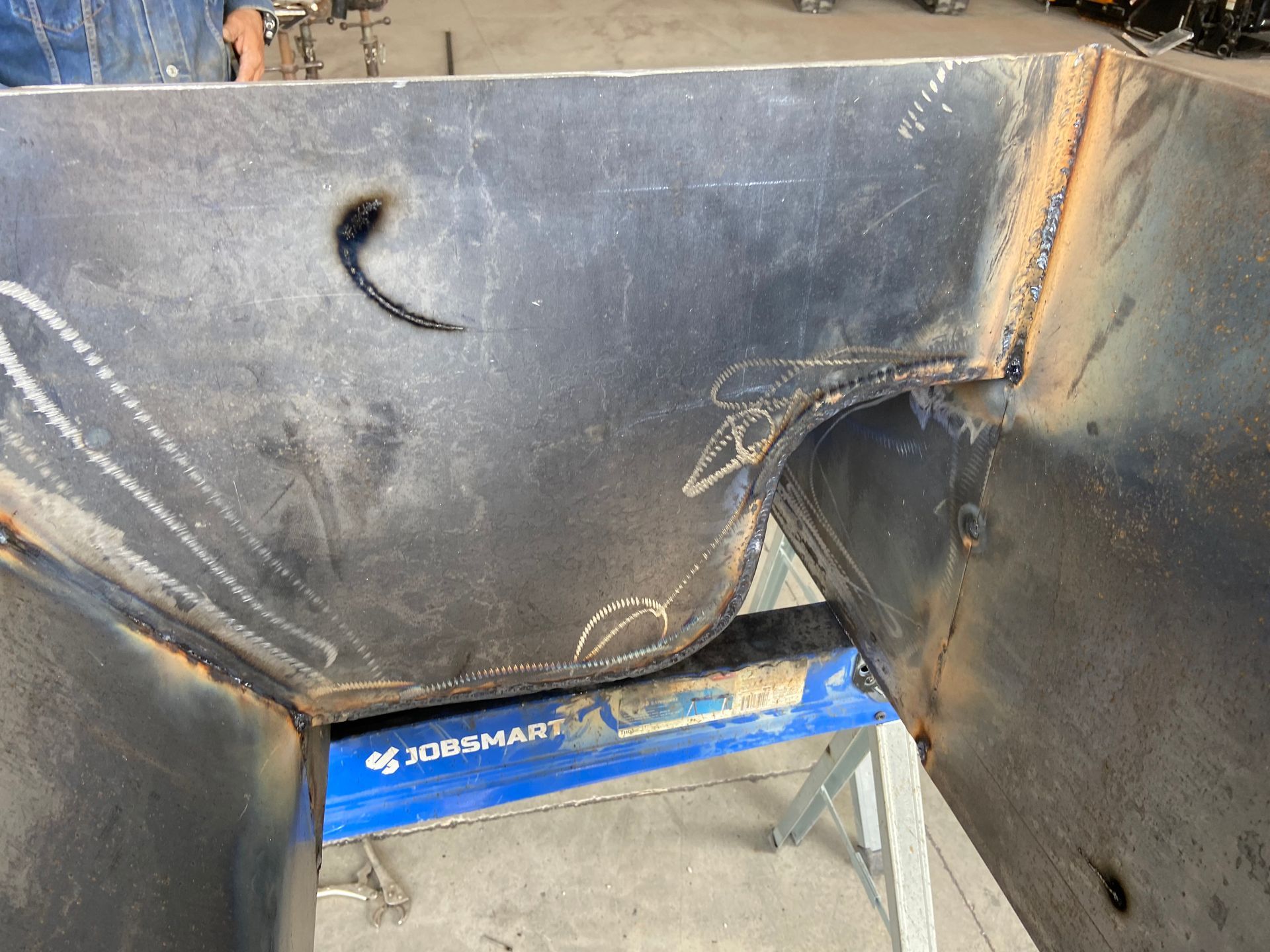 Welded metal structure with visible seams and a curved cutout, sitting on a blue workbench.